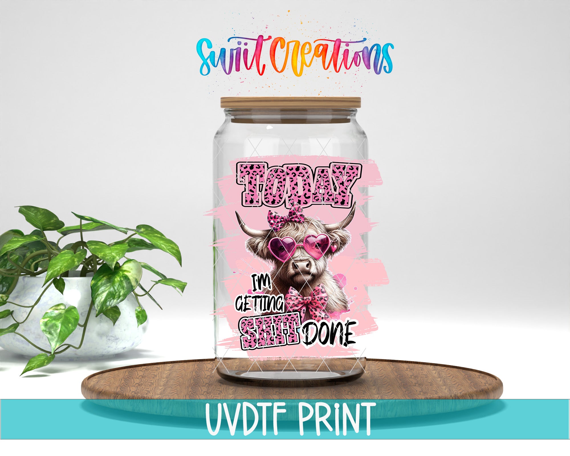 A clear glass jar with a printed design featuring a cow wearing sunglasses and the text "Today I'm getting done" printed on it. The jar is placed on a wooden surface, and there is a potted plant in the background.