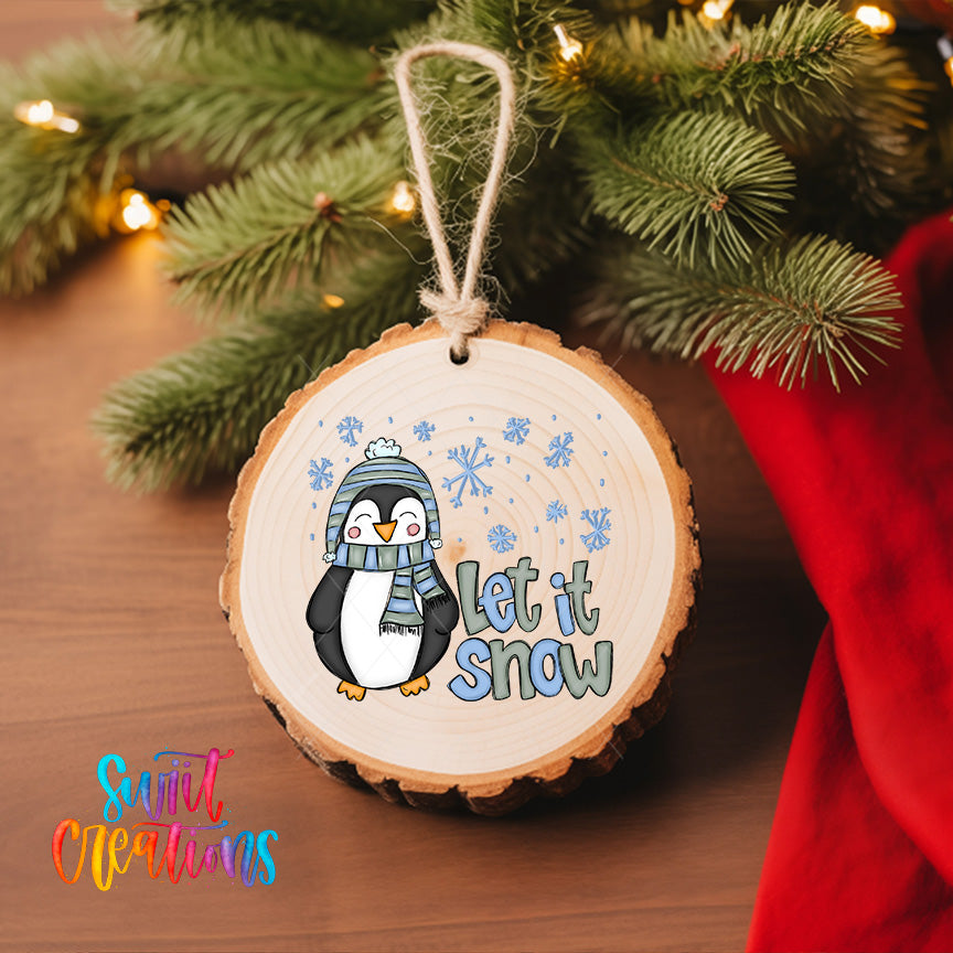 A wooden ornament with a penguin wearing a scarf and hat, surrounded by snowflakes, hangs on a Christmas tree.