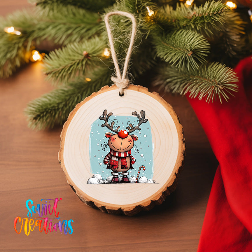 A wooden ornament featuring a cartoon reindeer with antlers, wearing a red scarf and standing on a snowy surface, is hanging on a Christmas tree.
