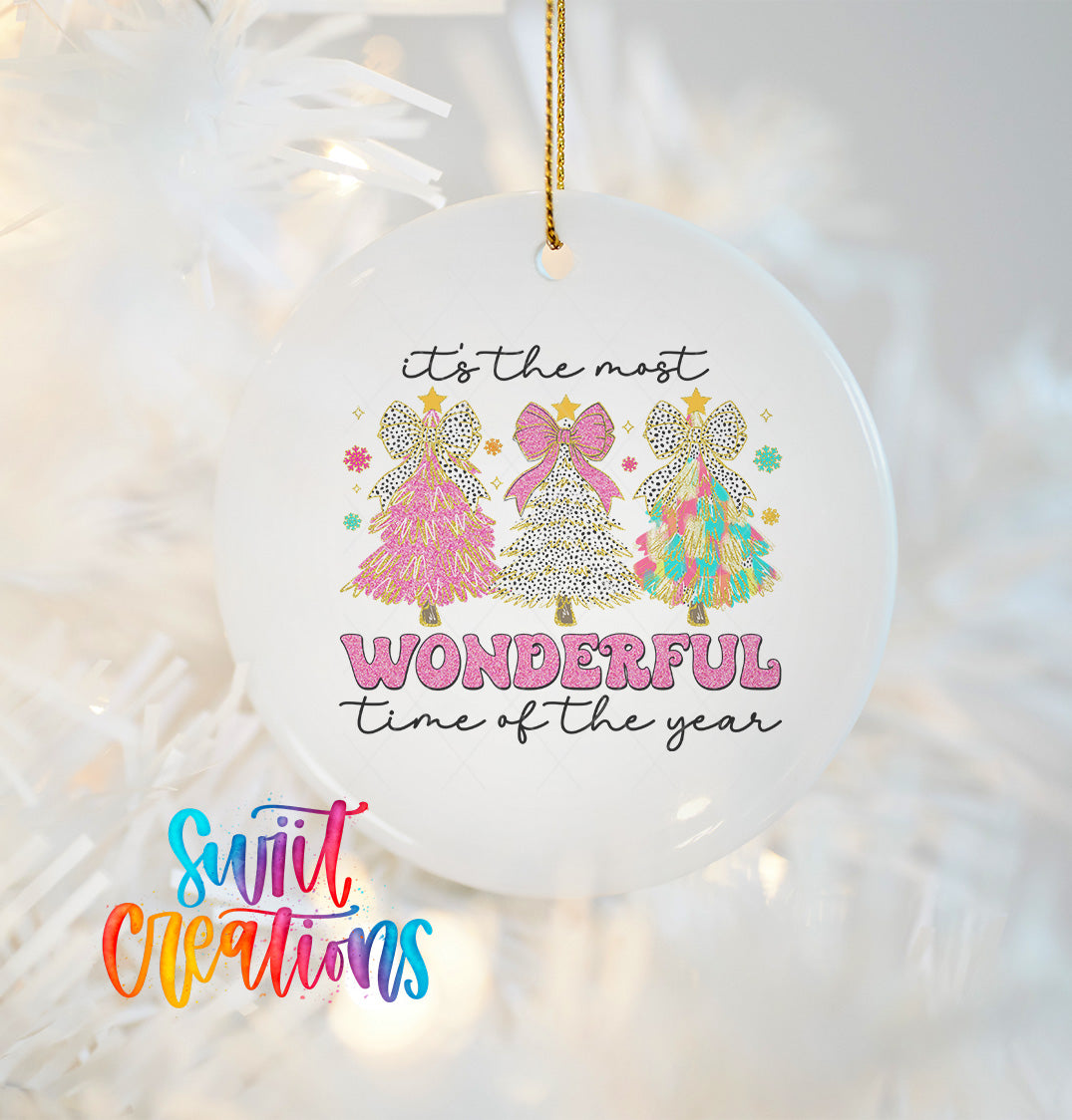 A white ornament with a festive design featuring three colorful Christmas trees and the text "It's the most WONDERFUL time of the year" hanging from a string.