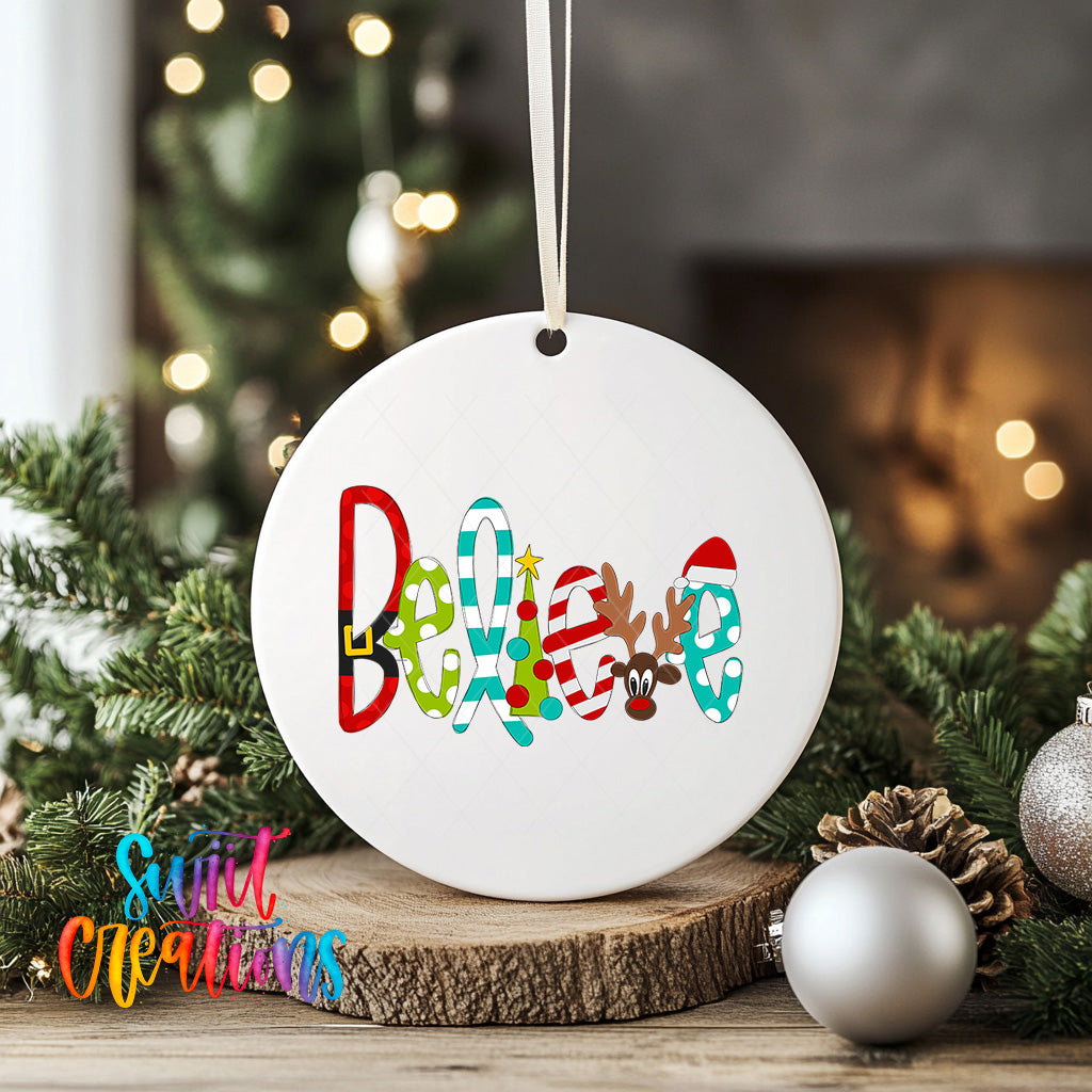 A white ceramic ornament with the word "Believe" written on it, surrounded by Christmas decorations such as pine branches, ornaments, and a string of lights.