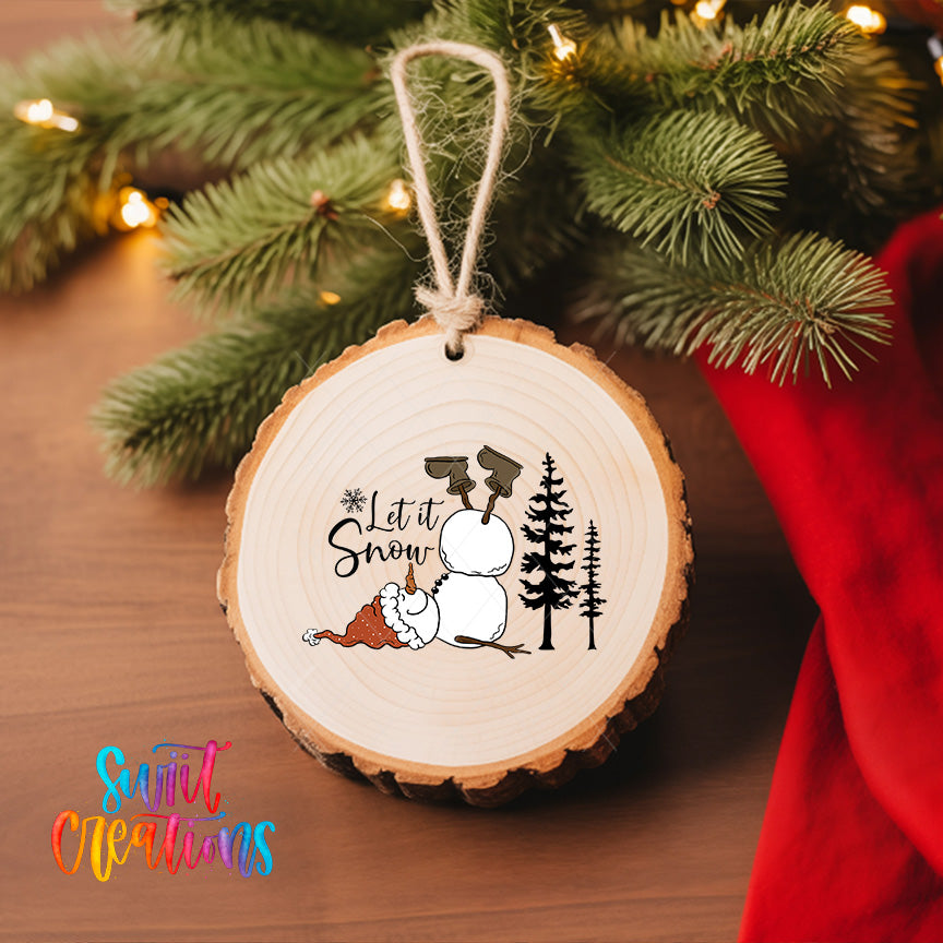 A wooden ornament with a snowman and pine trees, along with the text "Let it Snow" is hanging on a Christmas tree.