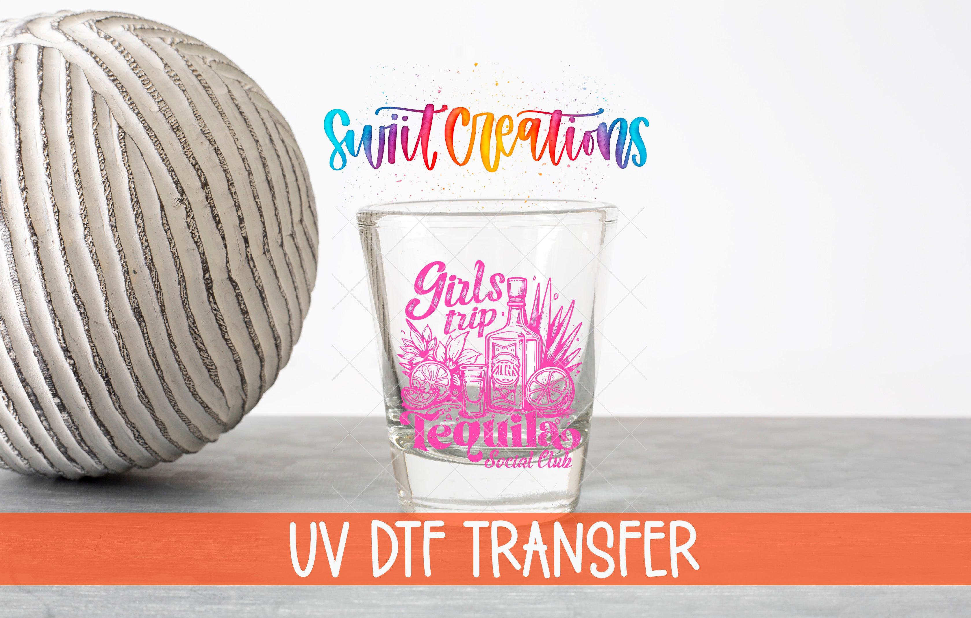 a shot glass with a colorful design and text, placed next to a gray ball on a table.