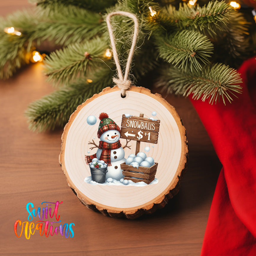 A wooden ornament featuring a snowman and a sign that says "Snowballs $1" is hanging on a Christmas tree.