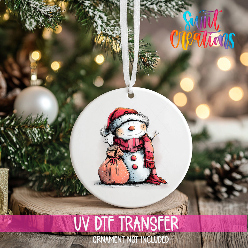 A white ceramic ornament featuring a snowman is hanging on a Christmas tree, with a blurred background of pine branches and twinkling lights.