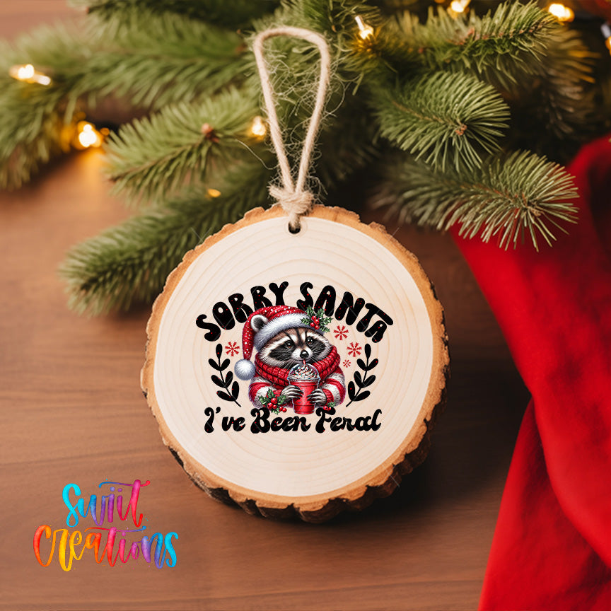 A wooden ornament with a raccoon wearing a Santa hat and the text "Sorry Santa, I've been fired" hanging on a Christmas tree.