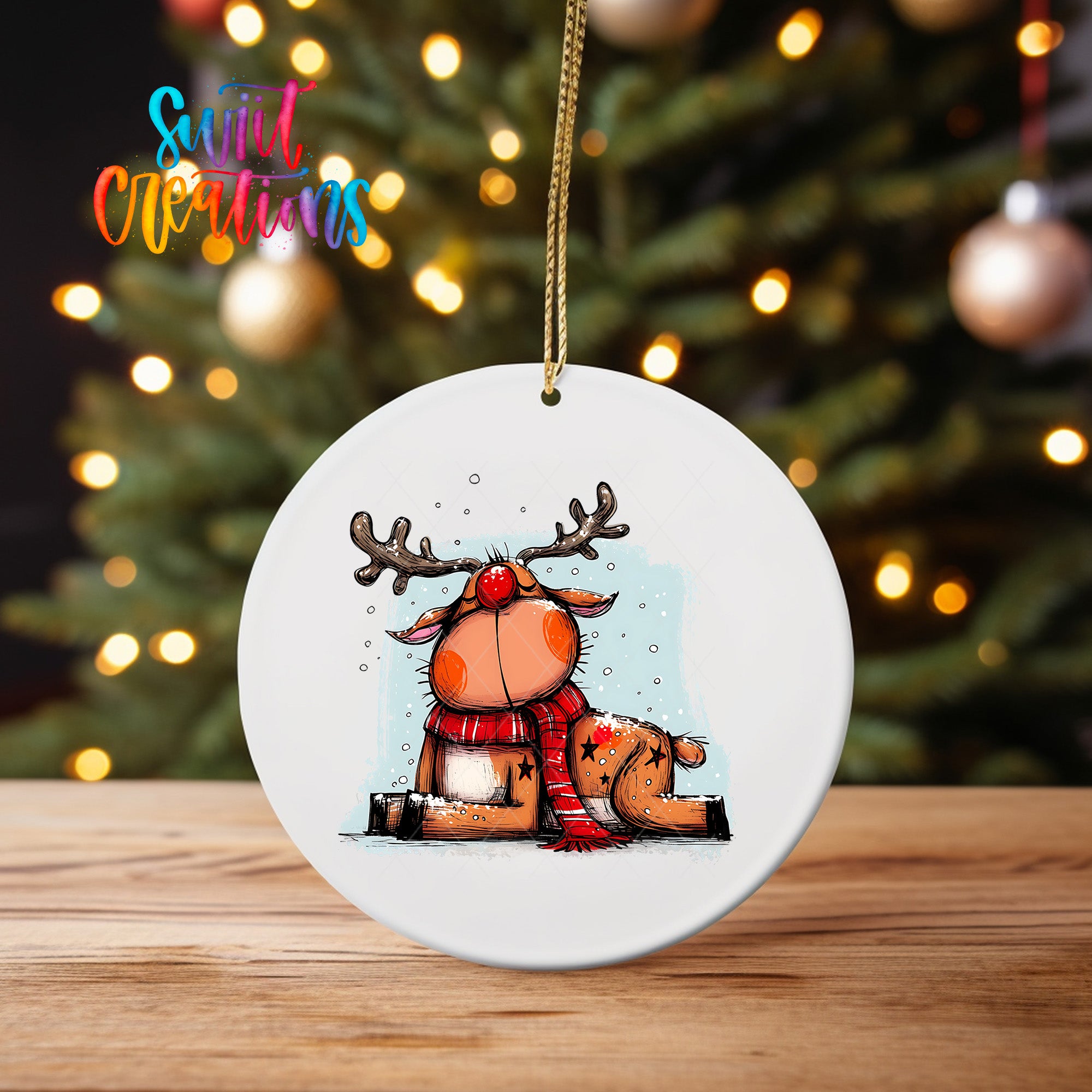 A white oval ornament featuring a cartoon reindeer with antlers and a red scarf, sitting on a wooden surface in front of a blurred Christmas tree with twinkling lights.