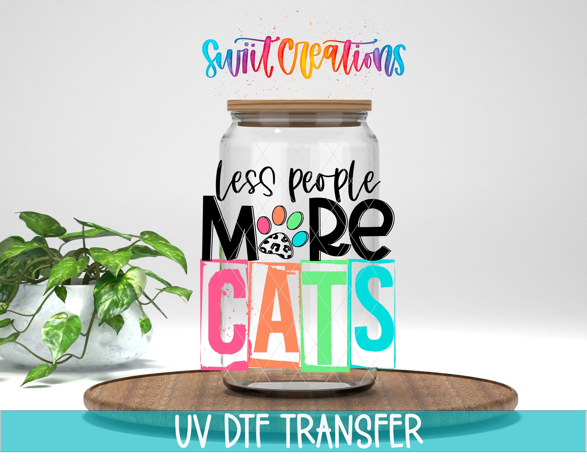 A jar with a lid, featuring a colorful and playful design with the text "less people more cats" and a paw print. The jar is placed on a wooden surface, and there is a potted plant in the background.