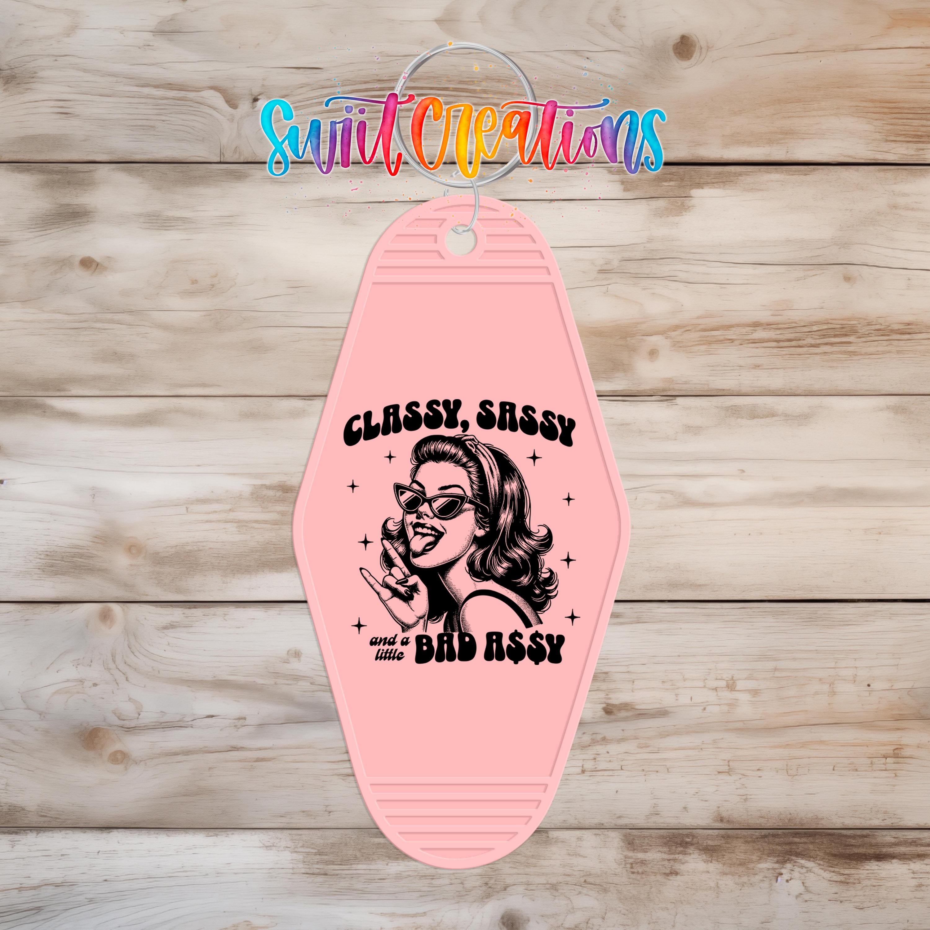 A pink keychain with a graphic design featuring a woman's face and the text "CLASSY, SASSY and a little BAD ASSY" printed on it.