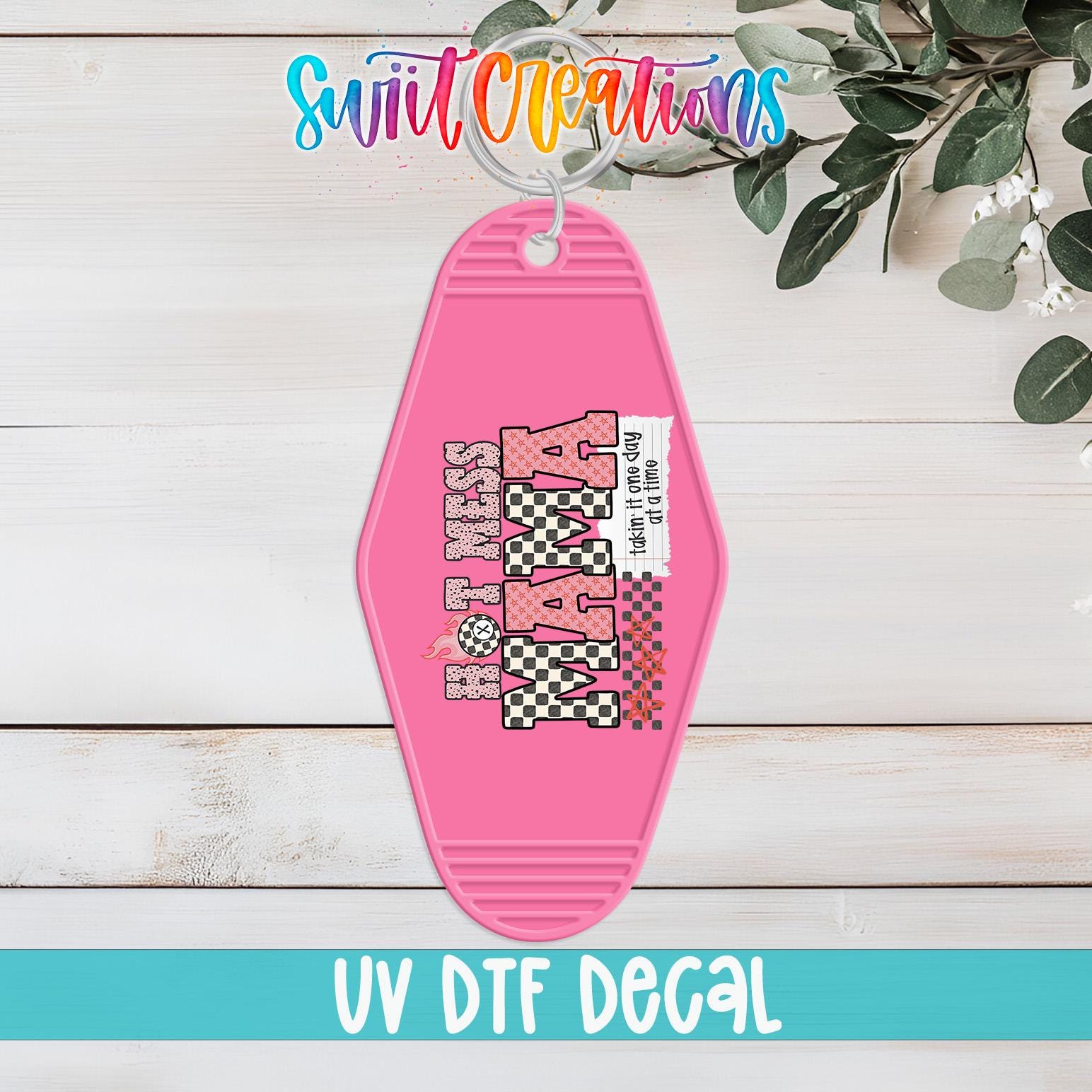 A pink keychain with the text "KARA" printed on it, hanging on a wooden surface with some greenery in the background.