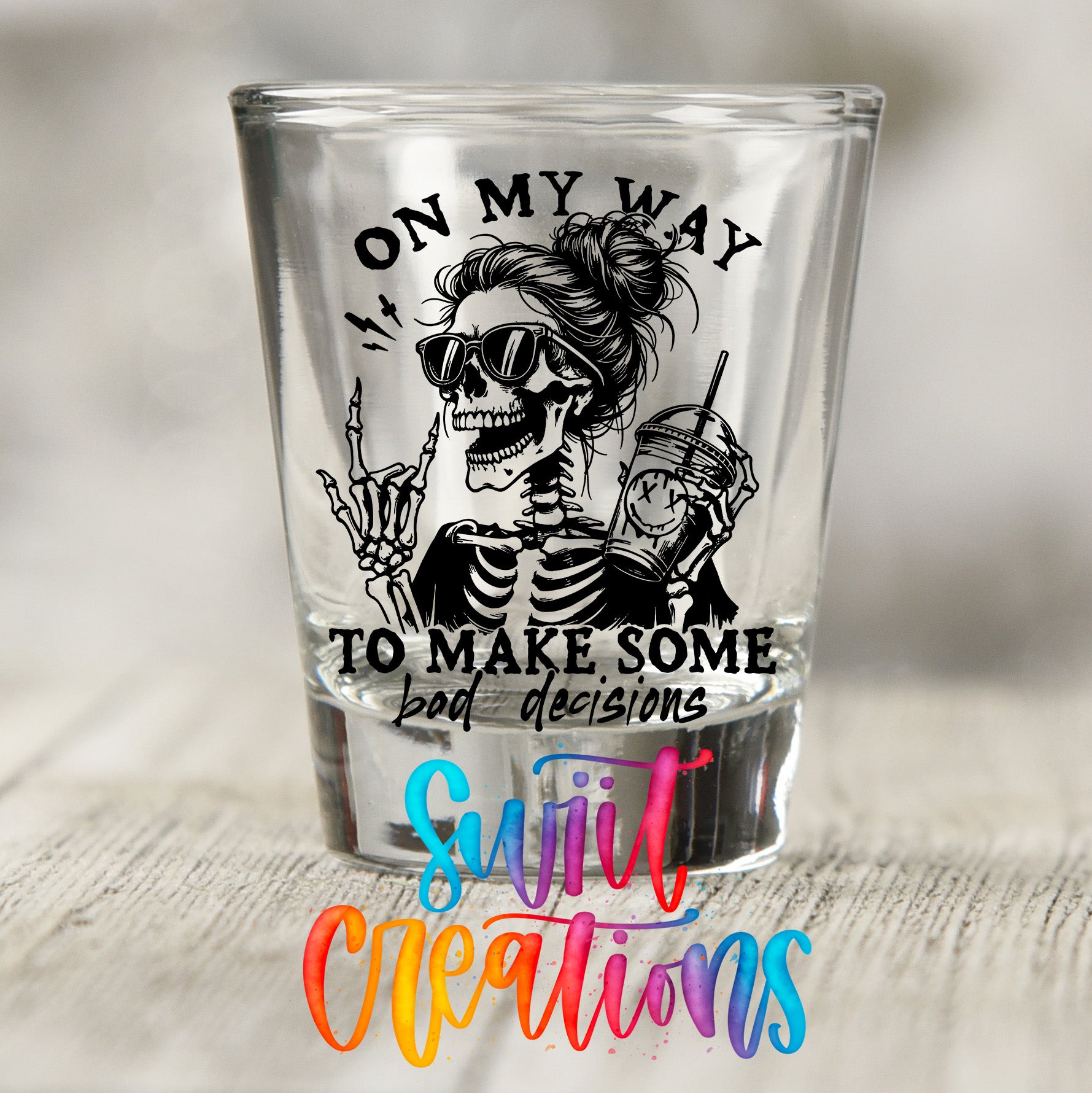 A shot glass with a graphic design featuring a skeleton wearing sunglasses and holding a drink, along with the text "ON MY WAY TO MAKE SOME BAD DECISIONS" and the phrase "Suit Creations" written below.