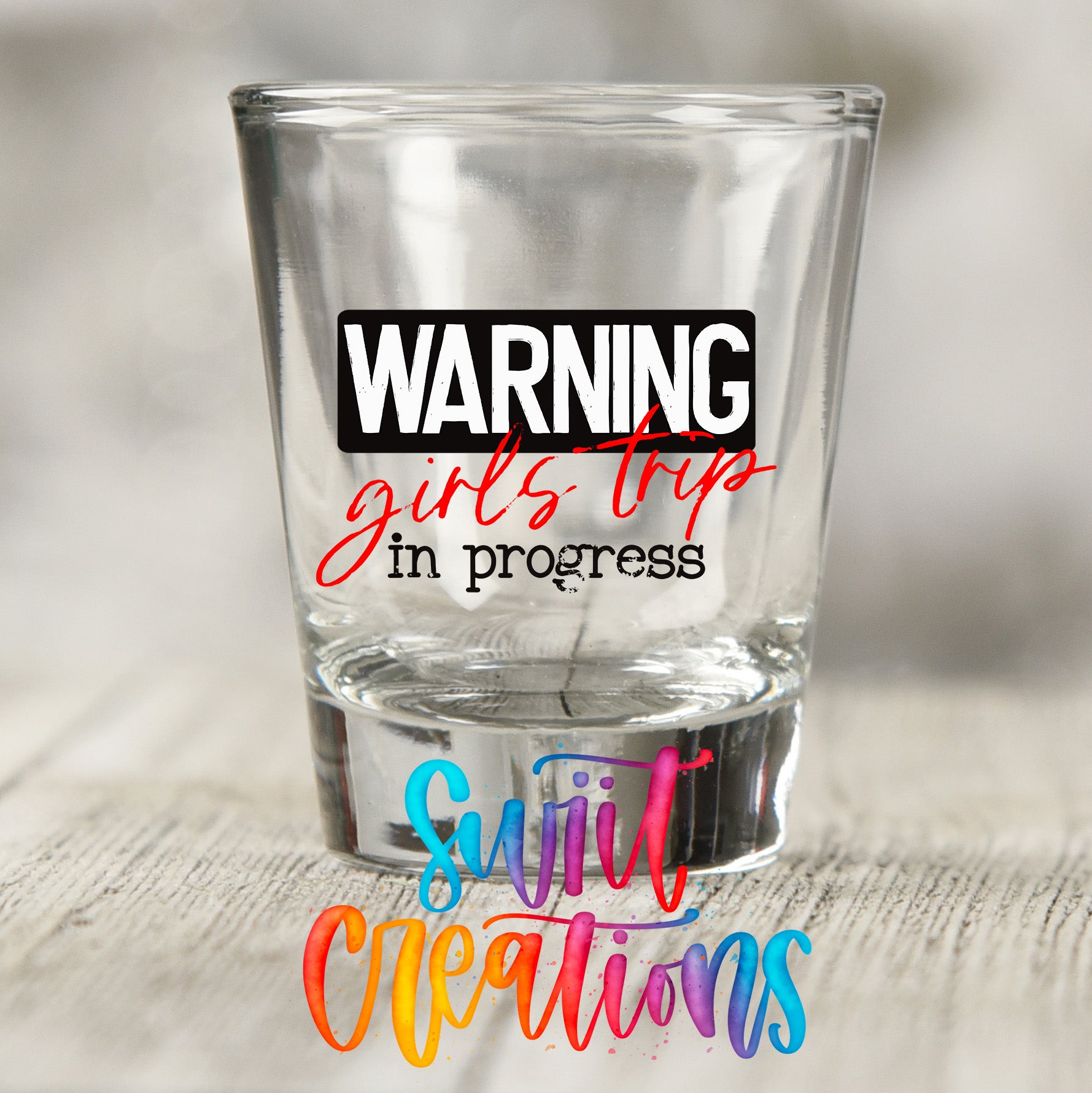 a clear shot glass with a bold, colorful text design on it.