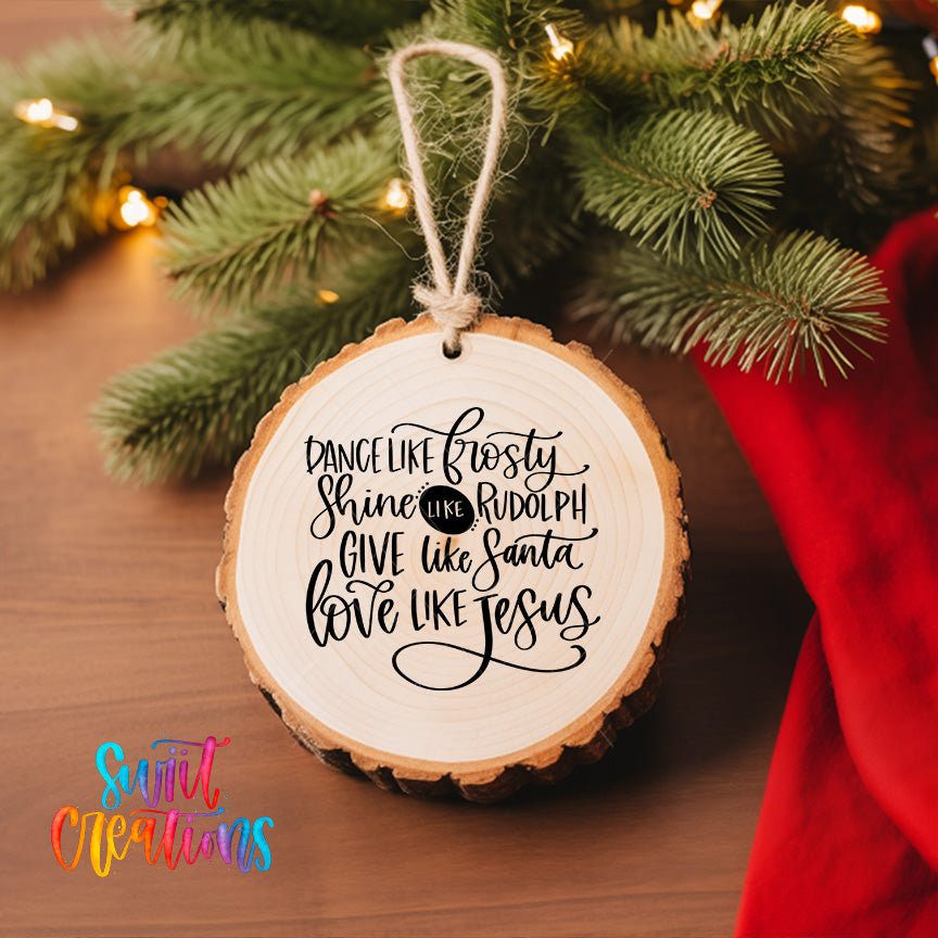 A wooden ornament with a hand-lettered quote hangs on a Christmas tree, surrounded by pine branches and twinkling lights.