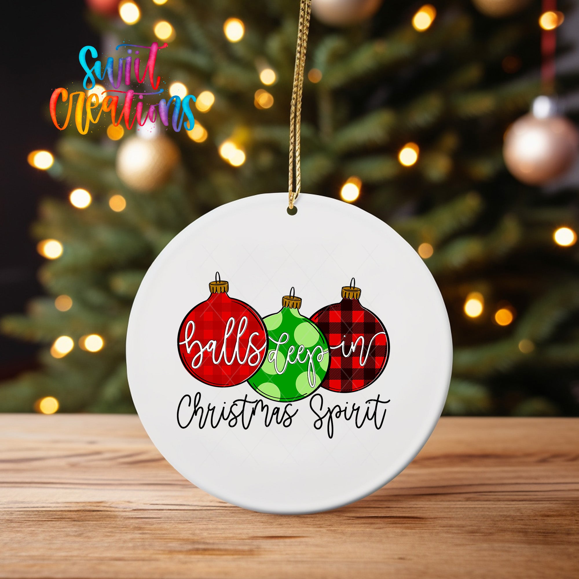 A white ceramic ornament with a festive design hangs on a wooden surface, featuring three Christmas ornaments with the text "balls go in Christmas spirit" written on them.