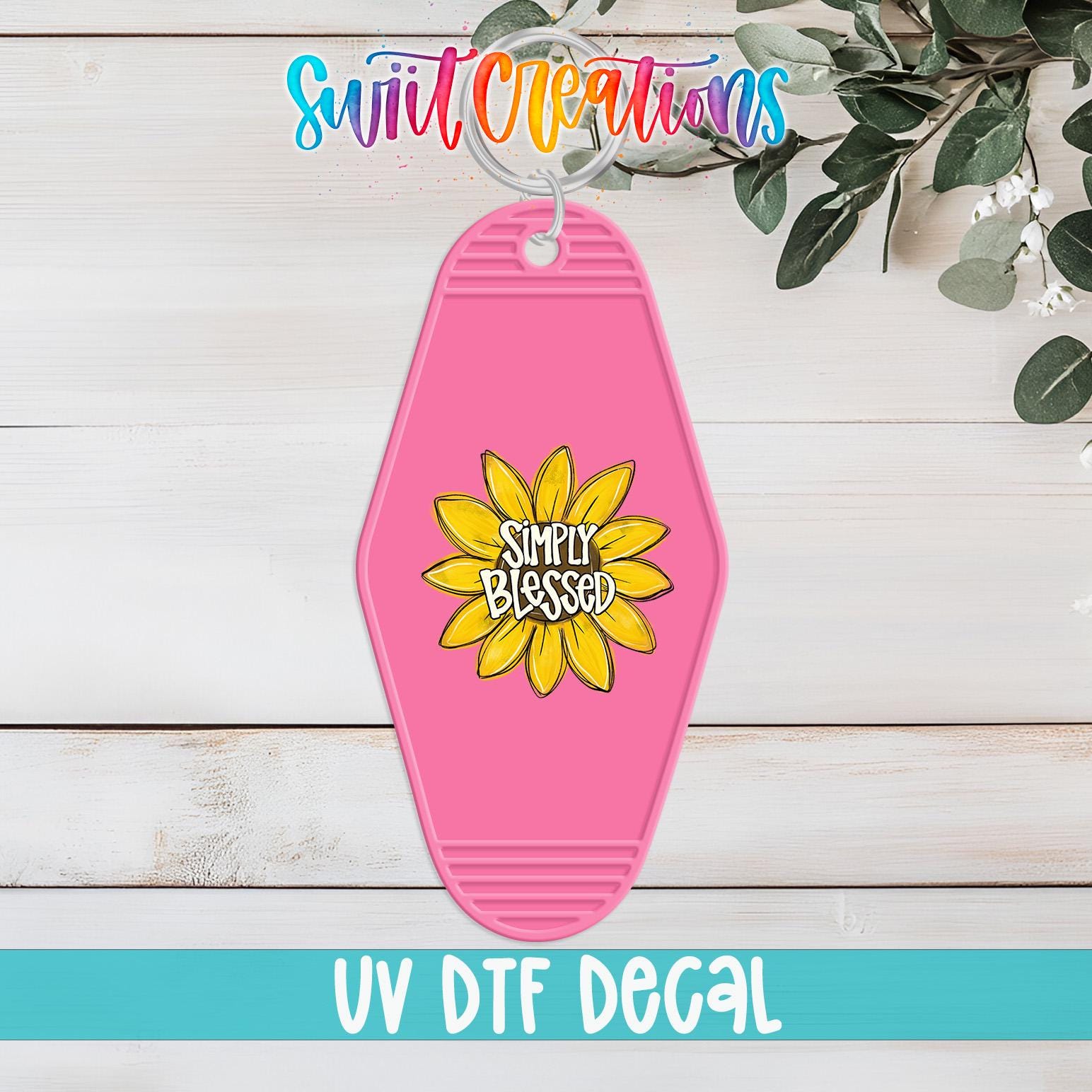 A pink keychain with a yellow flower design and the text "Simply Blessed" printed on it, hanging on a wooden surface.