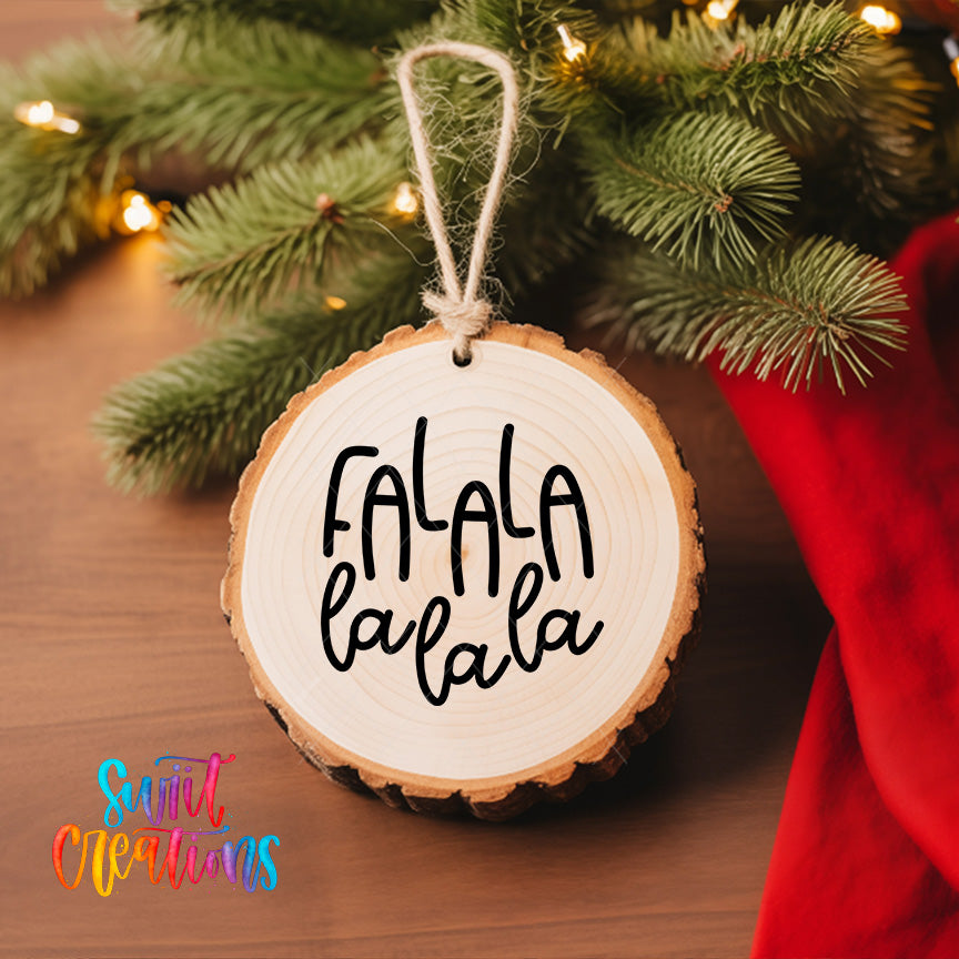 A wooden ornament with the text "FALA la la la" hanging from a tree branch, surrounded by pine branches and twinkling lights.