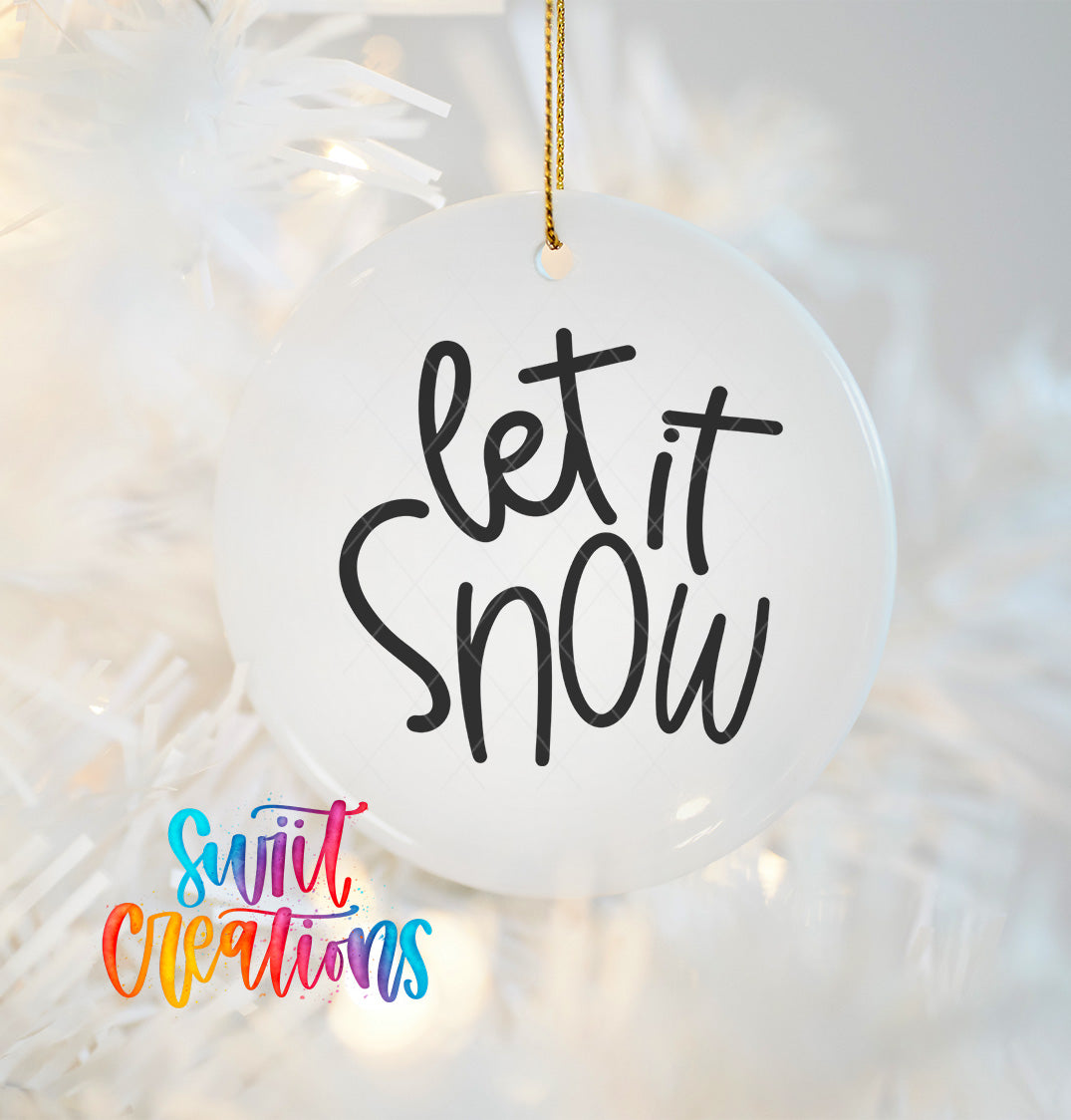A white ornament with the text "let it Snow" written on it, hanging on a white background with a blurred background that appears to be a Christmas tree.