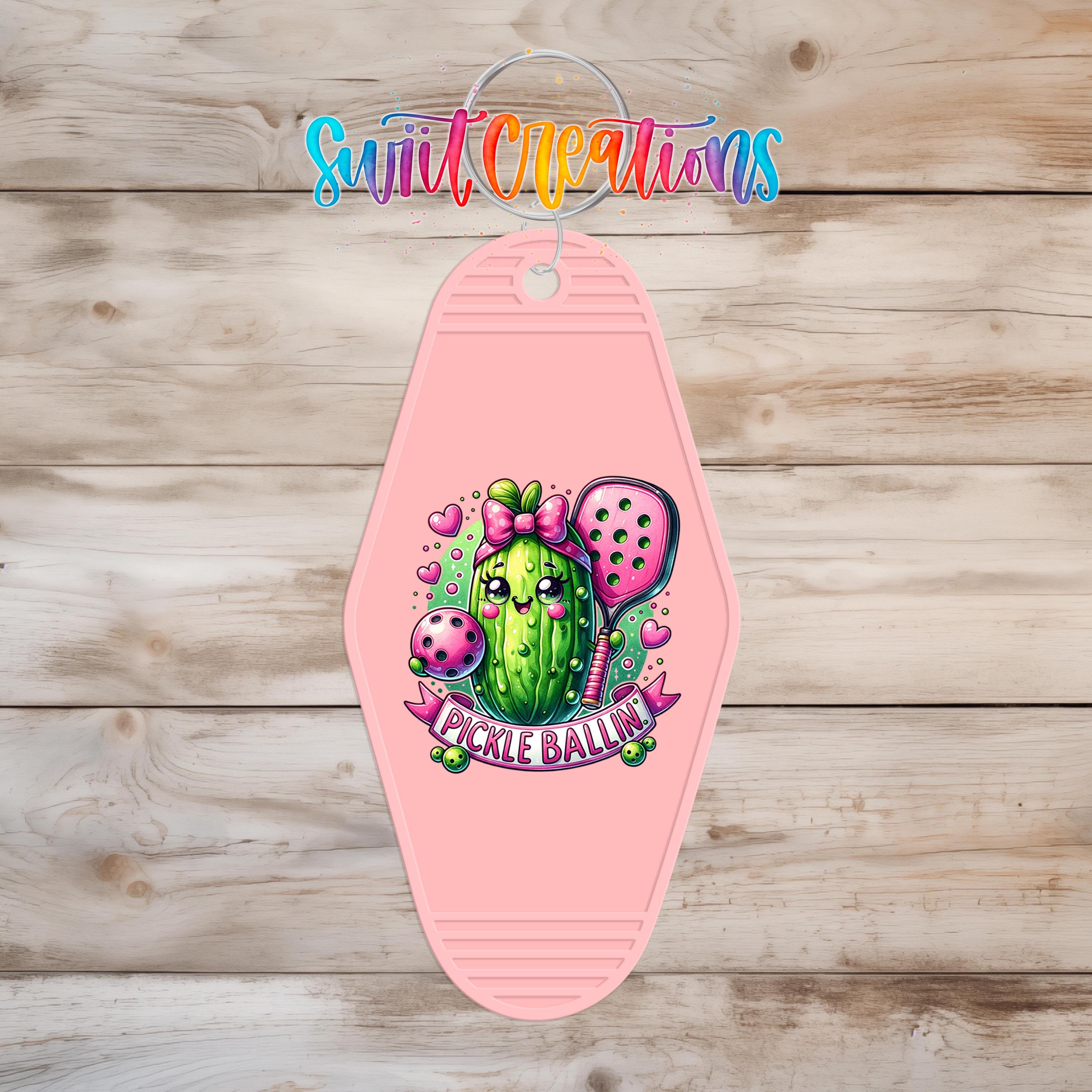 A pink keychain with a cartoon image of a pickle on it, along with the text "Pickle Ballin" and a bow.