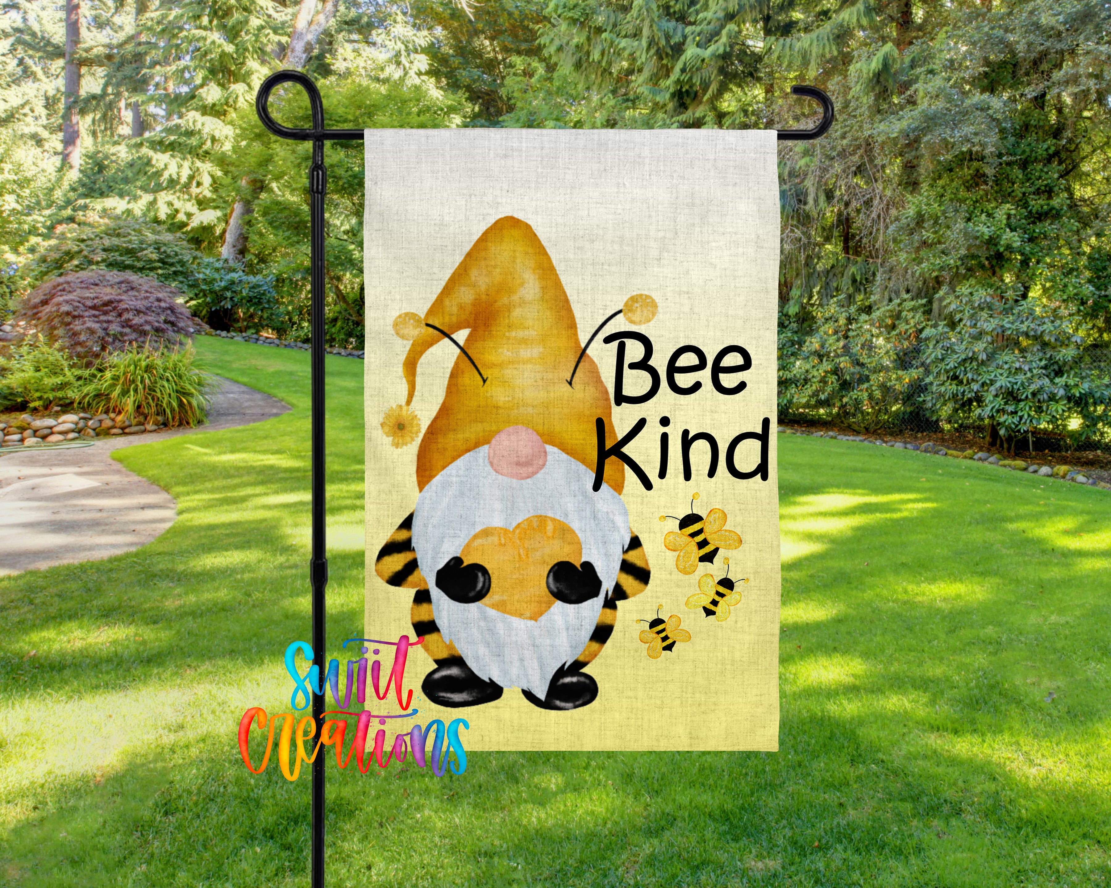 A garden gnome with a yellow hat and a sign that says "Bee Kind" is displayed in a grassy area surrounded by trees.