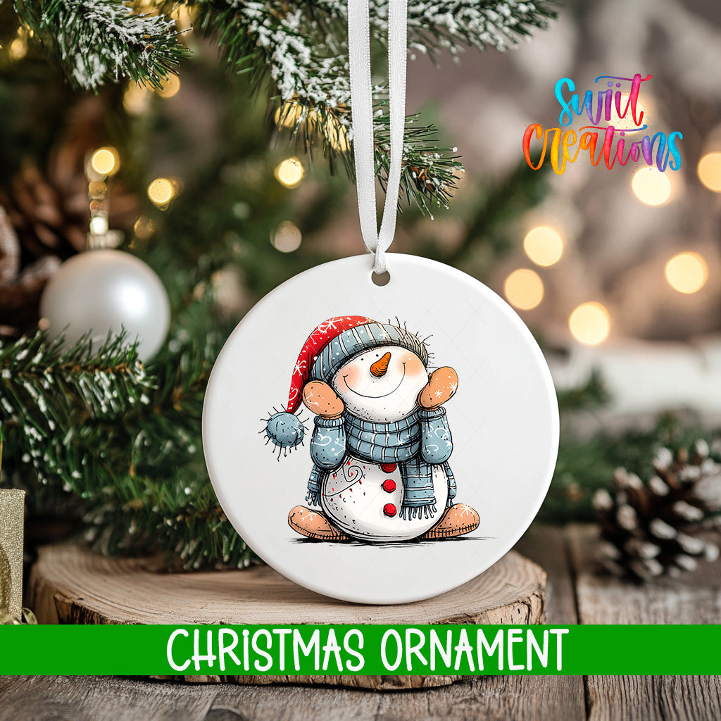 A white Christmas ornament featuring a snowman is hanging from a tree branch, with a blurred background of lights and greenery.