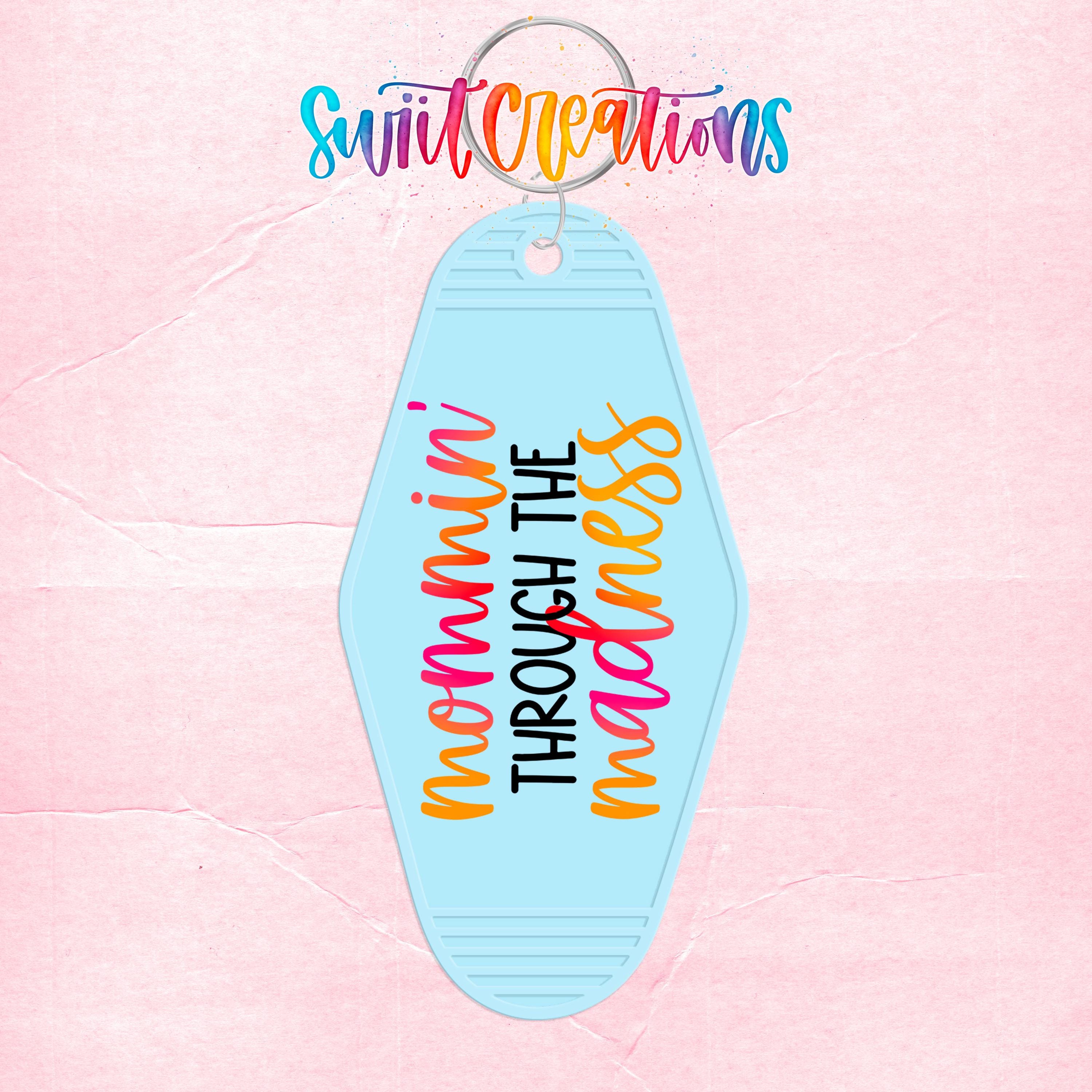A keychain with the text "mommini through the madness" printed on it, against a pink background.