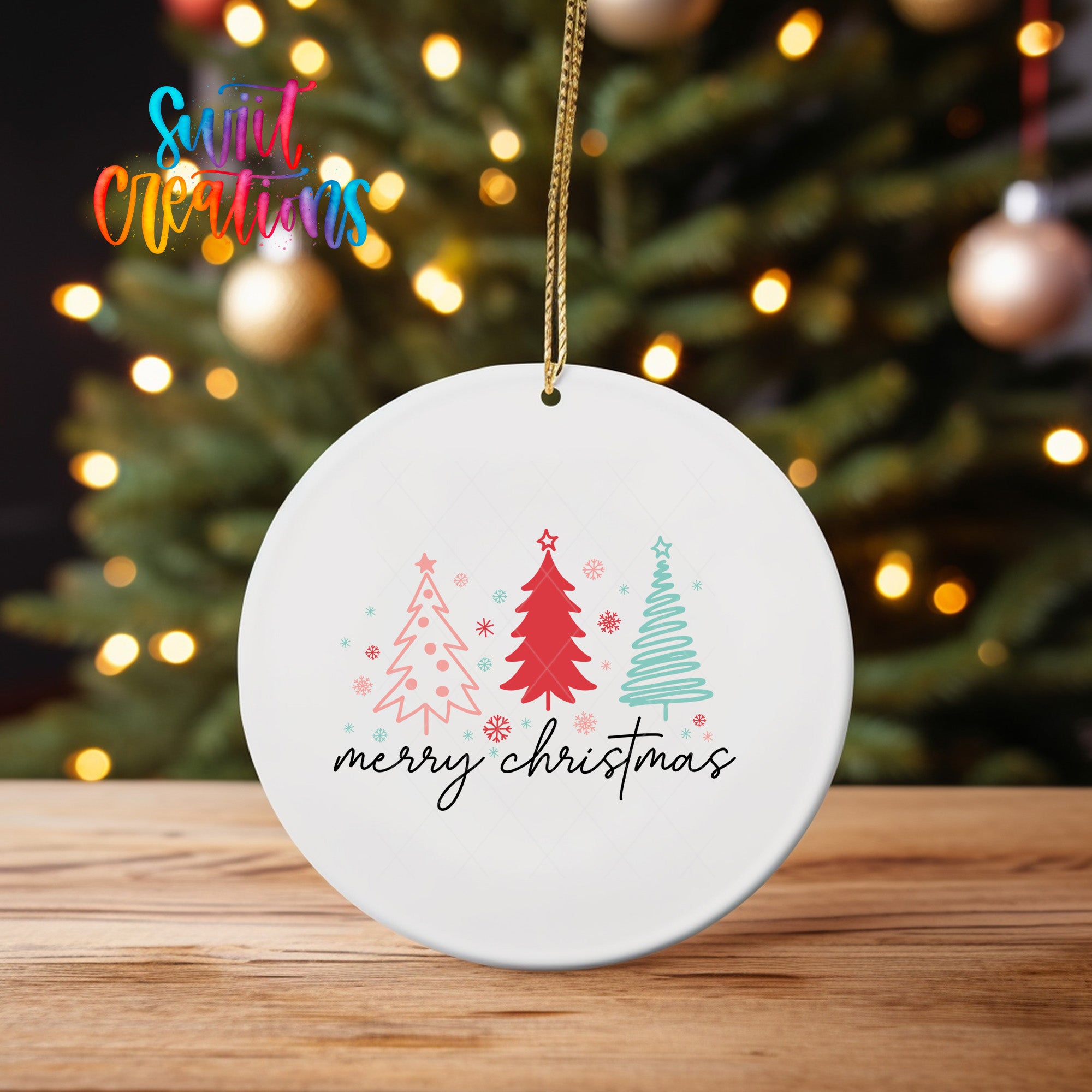 A white ceramic ornament with a festive design hangs on a wooden surface, featuring a Christmas tree and the text "Merry Christmas" in a stylized font.