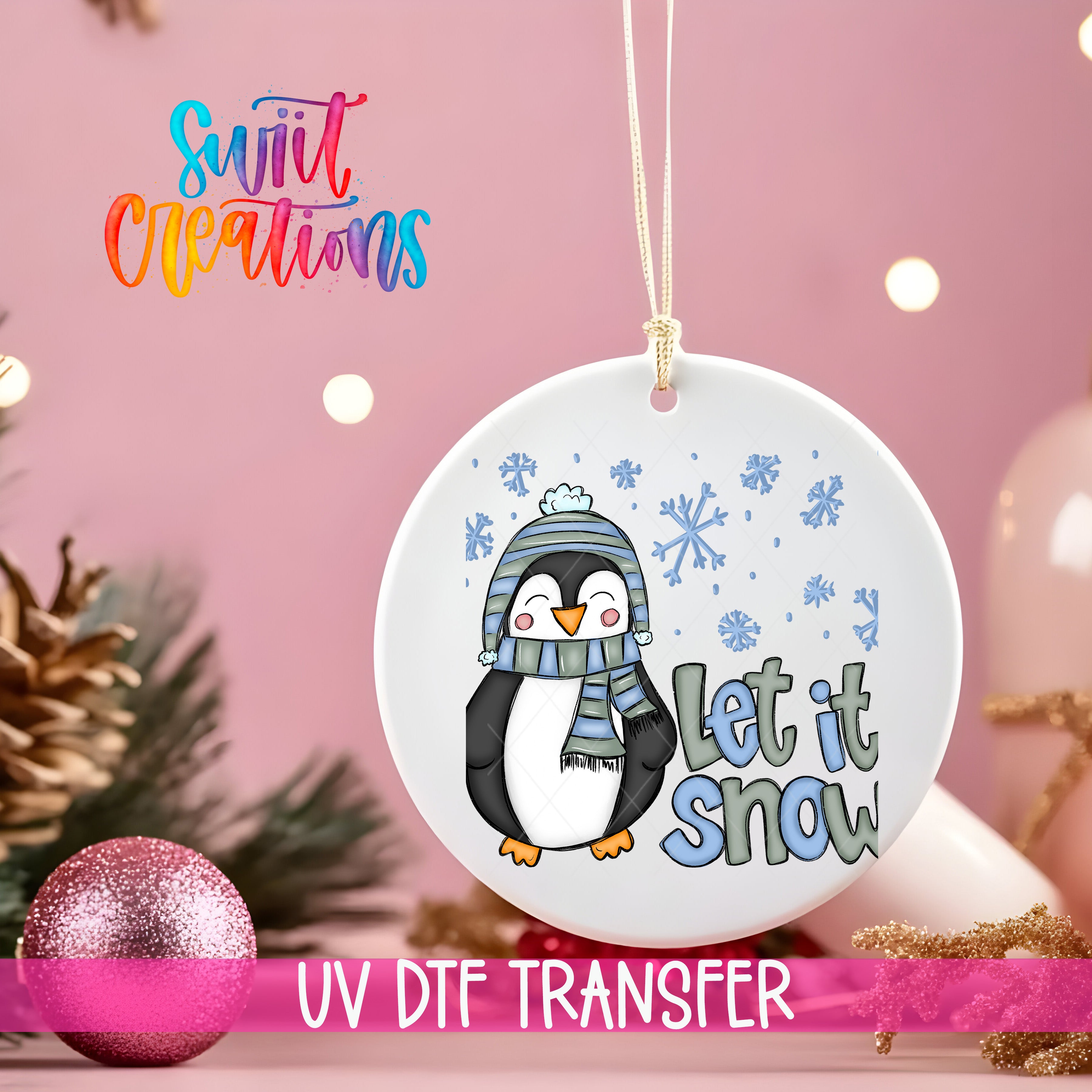 A white ornament with a penguin wearing a scarf and the text "Let it snow" is hanging on a string against a pink background.