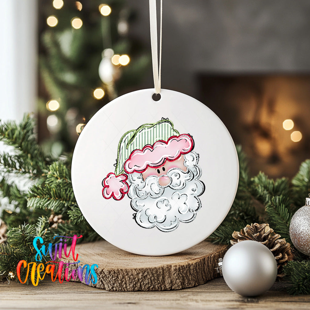 A white ceramic ornament with a Santa Claus face design is displayed on a wooden surface, surrounded by Christmas decorations and greenery.