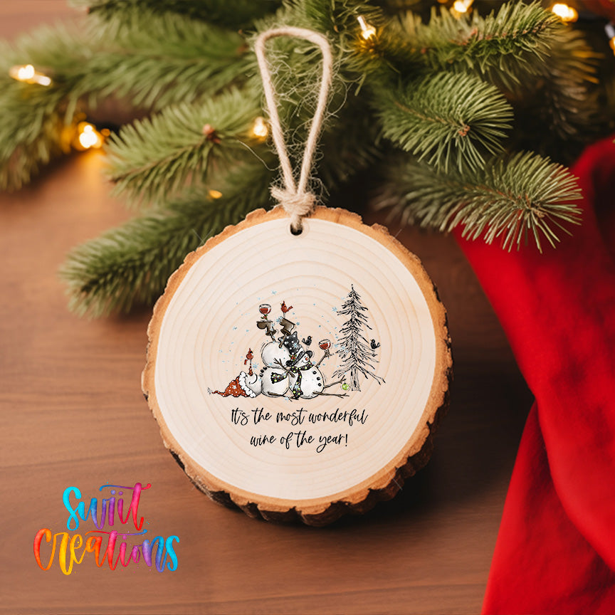 A wooden ornament with a snowman and pine trees, hanging on a Christmas tree.