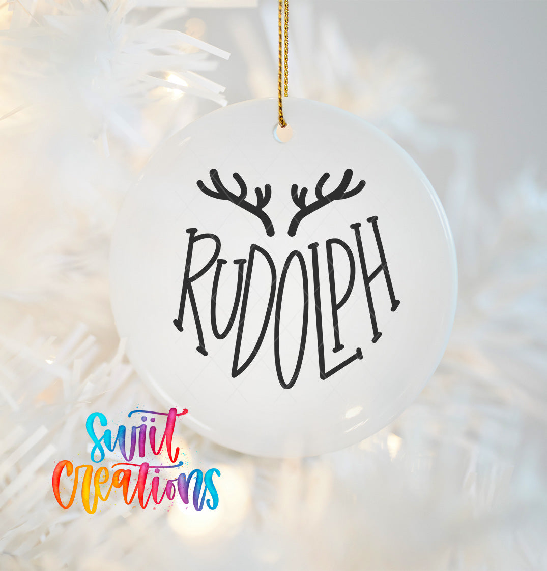 A white ornament with the word "RUDOLPH" written on it, hanging on a Christmas tree.