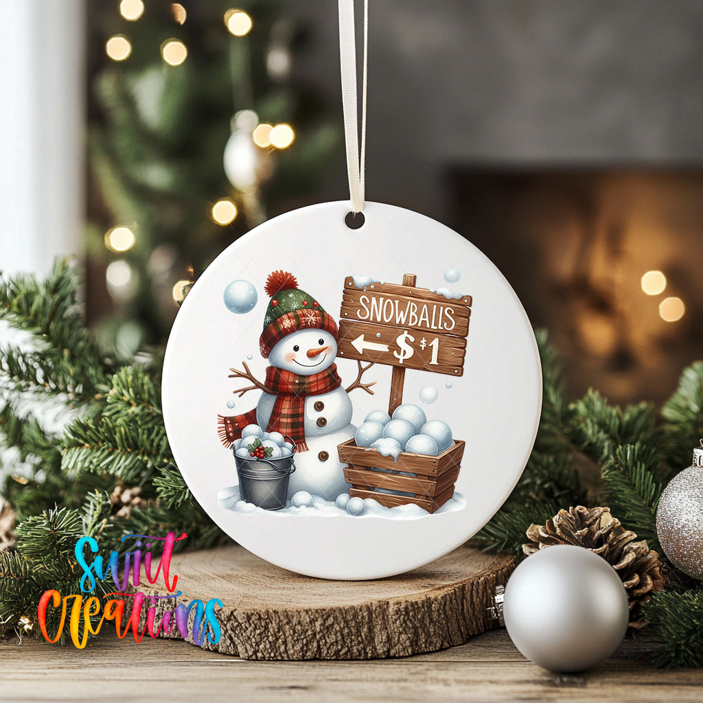 A white ceramic ornament featuring a snowman holding a sign that says "Snowballs $1" and a basket of snowballs, surrounded by Christmas decorations and greenery.