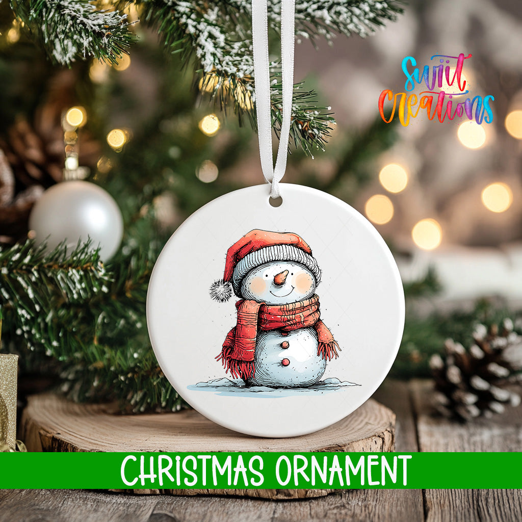 A white Christmas ornament featuring a snowman is hanging from a tree branch, with a blurred background of lights and greenery.