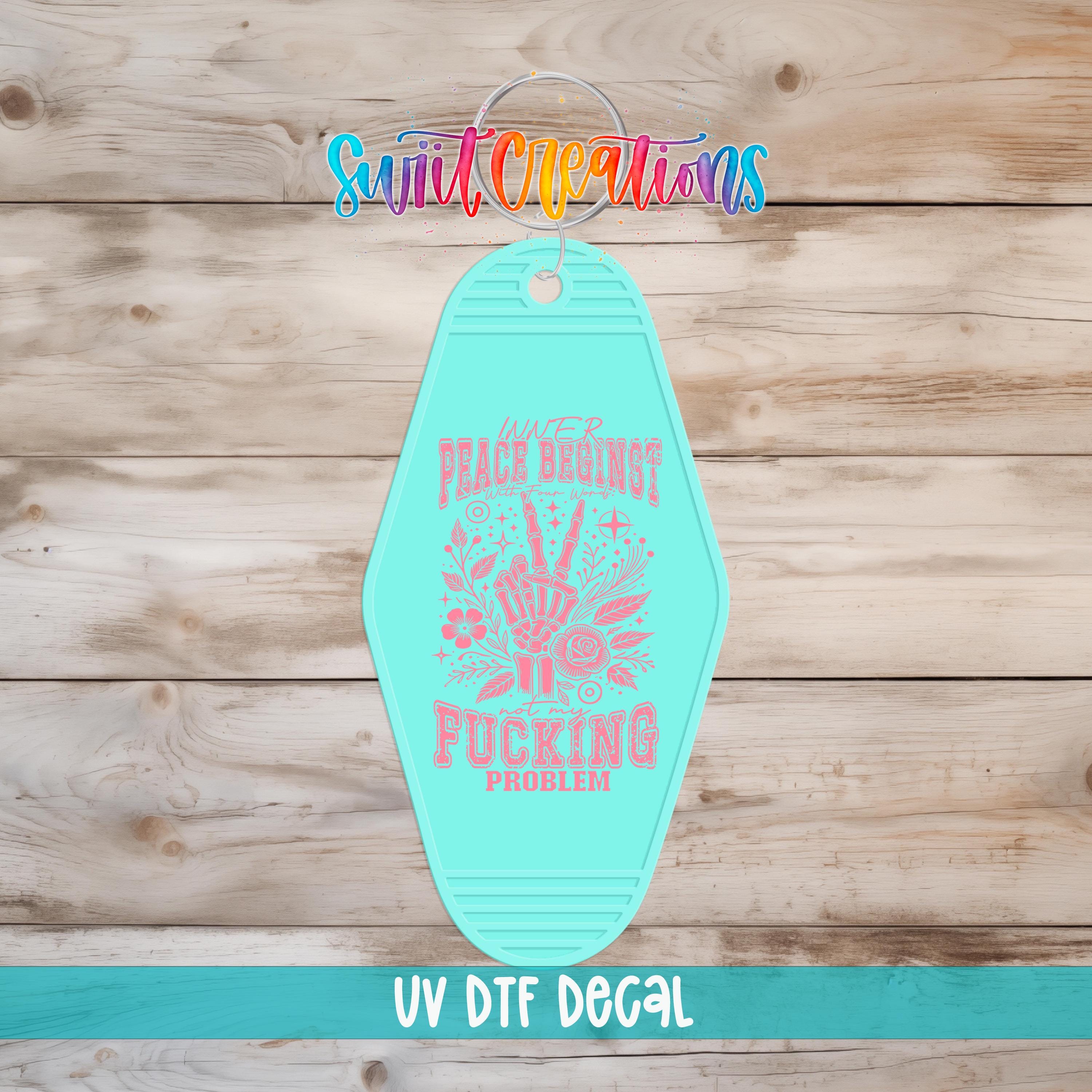 A turquoise keychain with a colorful design and text on it, placed on a wooden surface.