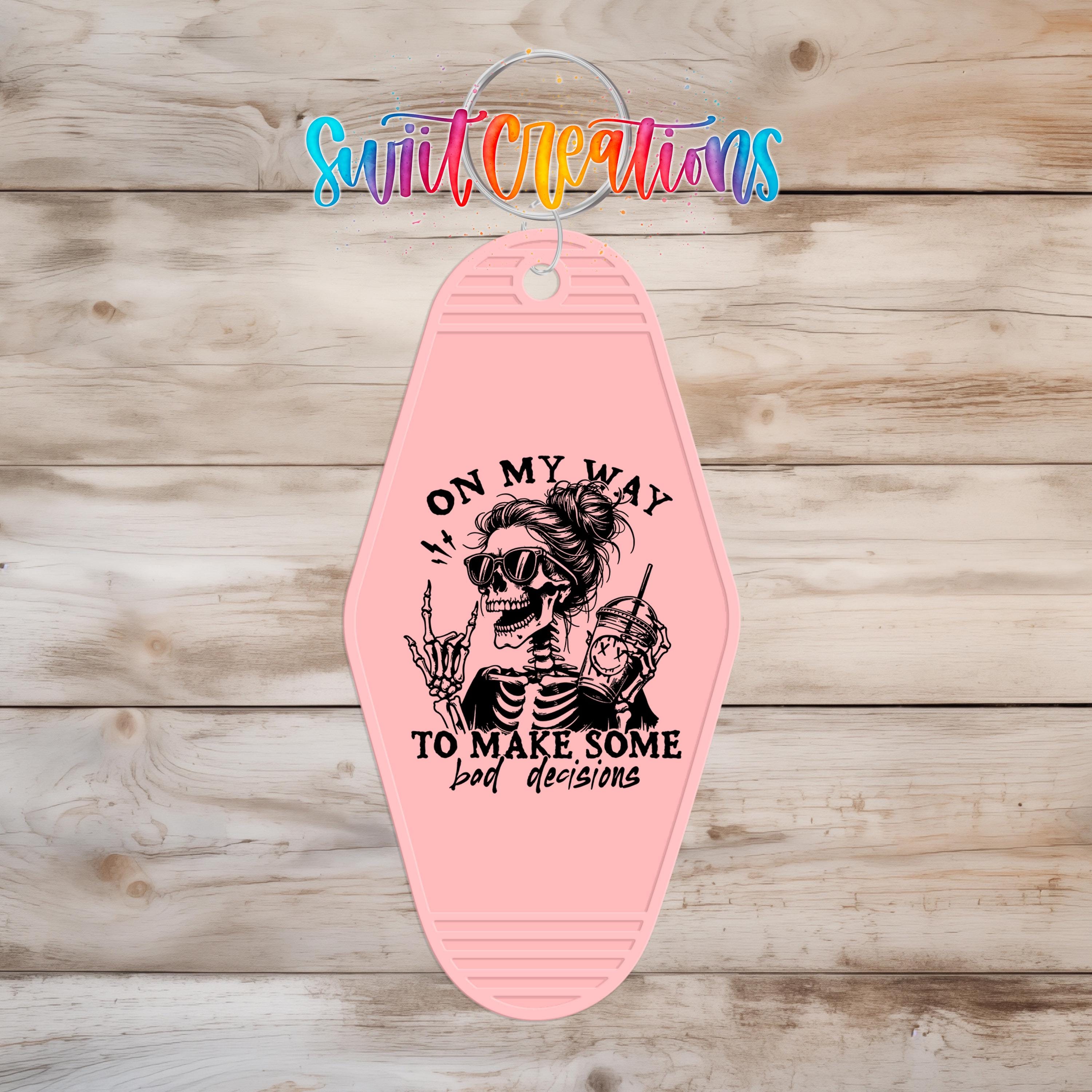 A pink keychain with a skeleton design and text that says "ON MY WAY TO MAKE SOME BAD DECISIONS".
