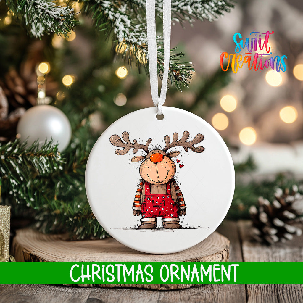 A white Christmas ornament featuring a cartoon reindeer is hanging on a tree branch, with a blurred background of pine branches and twinkling lights.