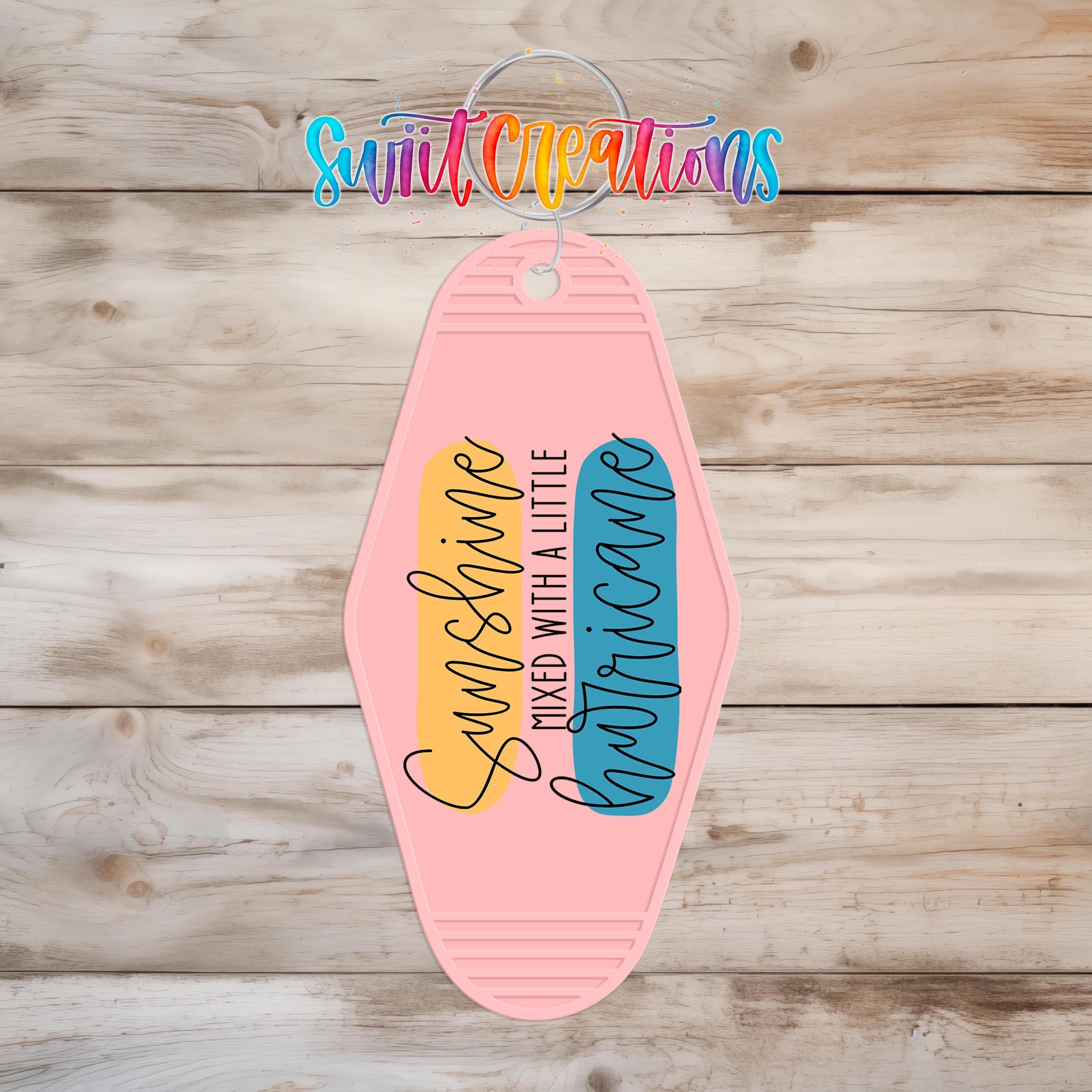 A pink keychain with a colorful design and text on it, hanging on a wooden surface.