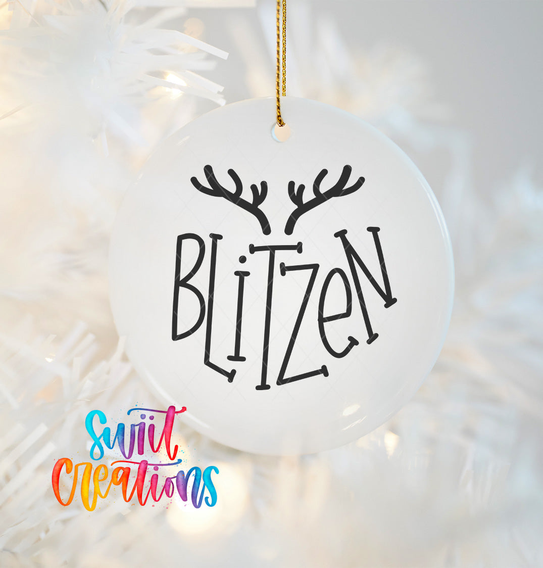 A white ornament with the word "BLITZEN" written on it, hanging on a Christmas tree.
