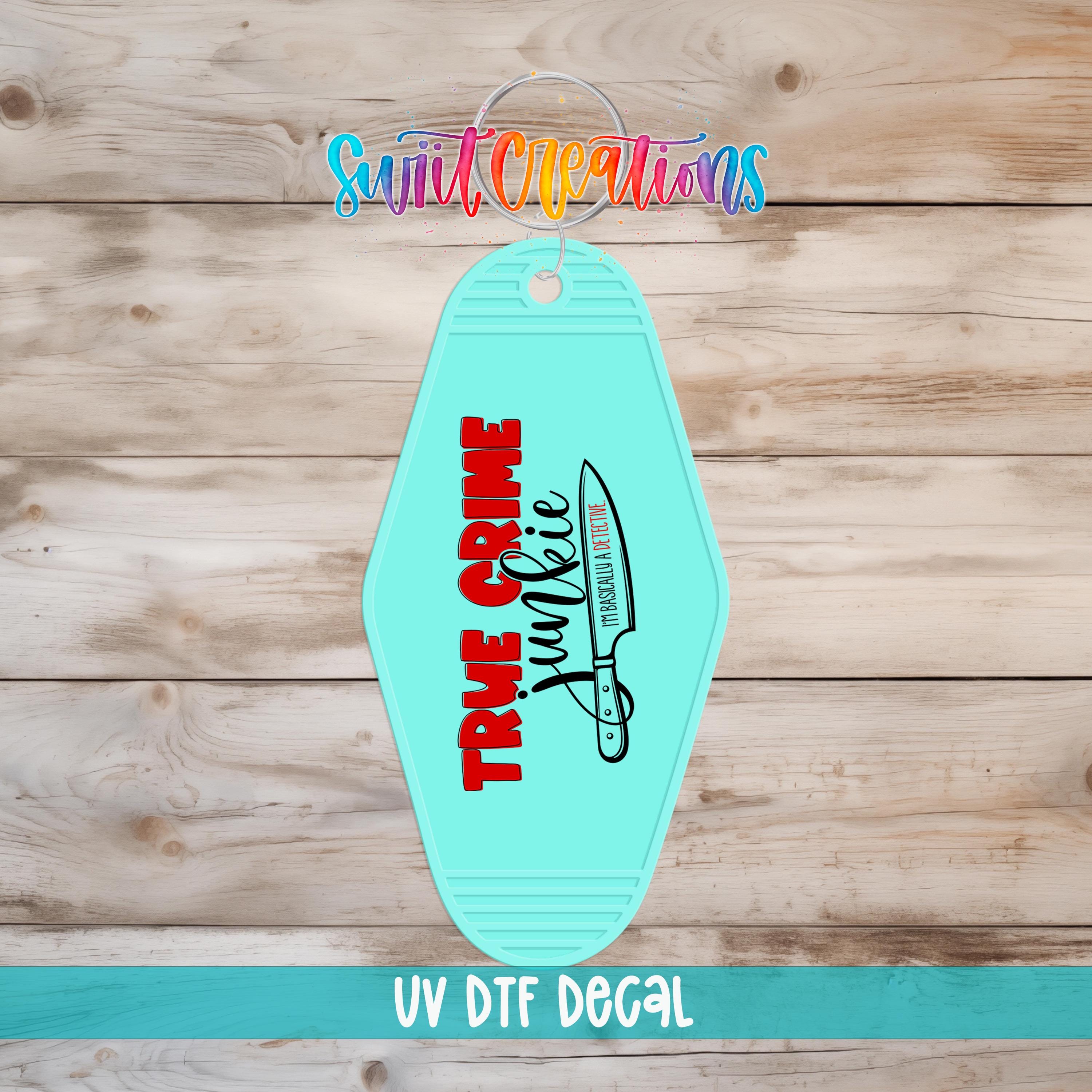 A turquoise keychain with the text "TRUE CRIME" and a graphic of a knife, displayed on a wooden surface.