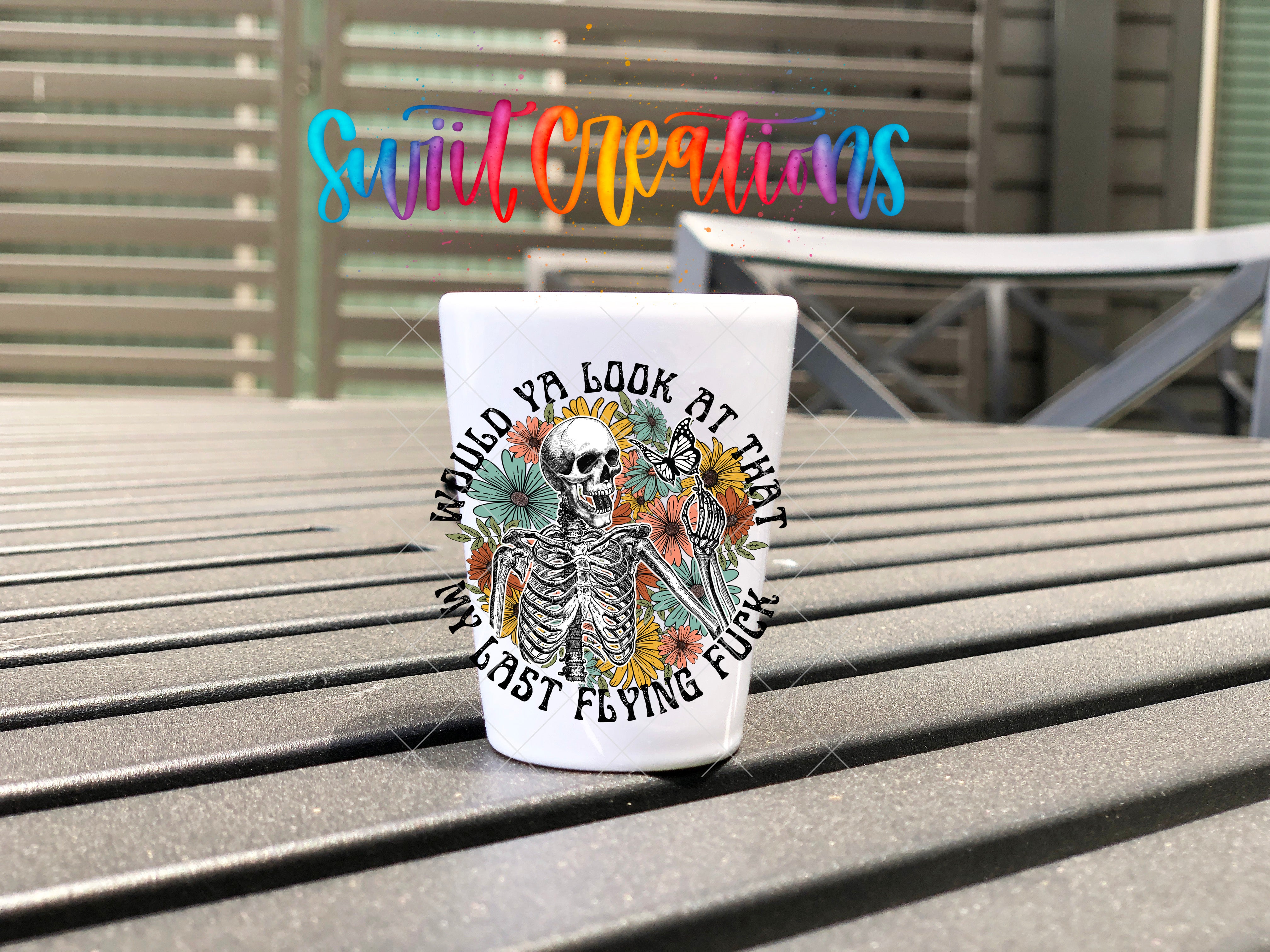 A white mug with a skeleton design and floral elements, placed on a metal bench.