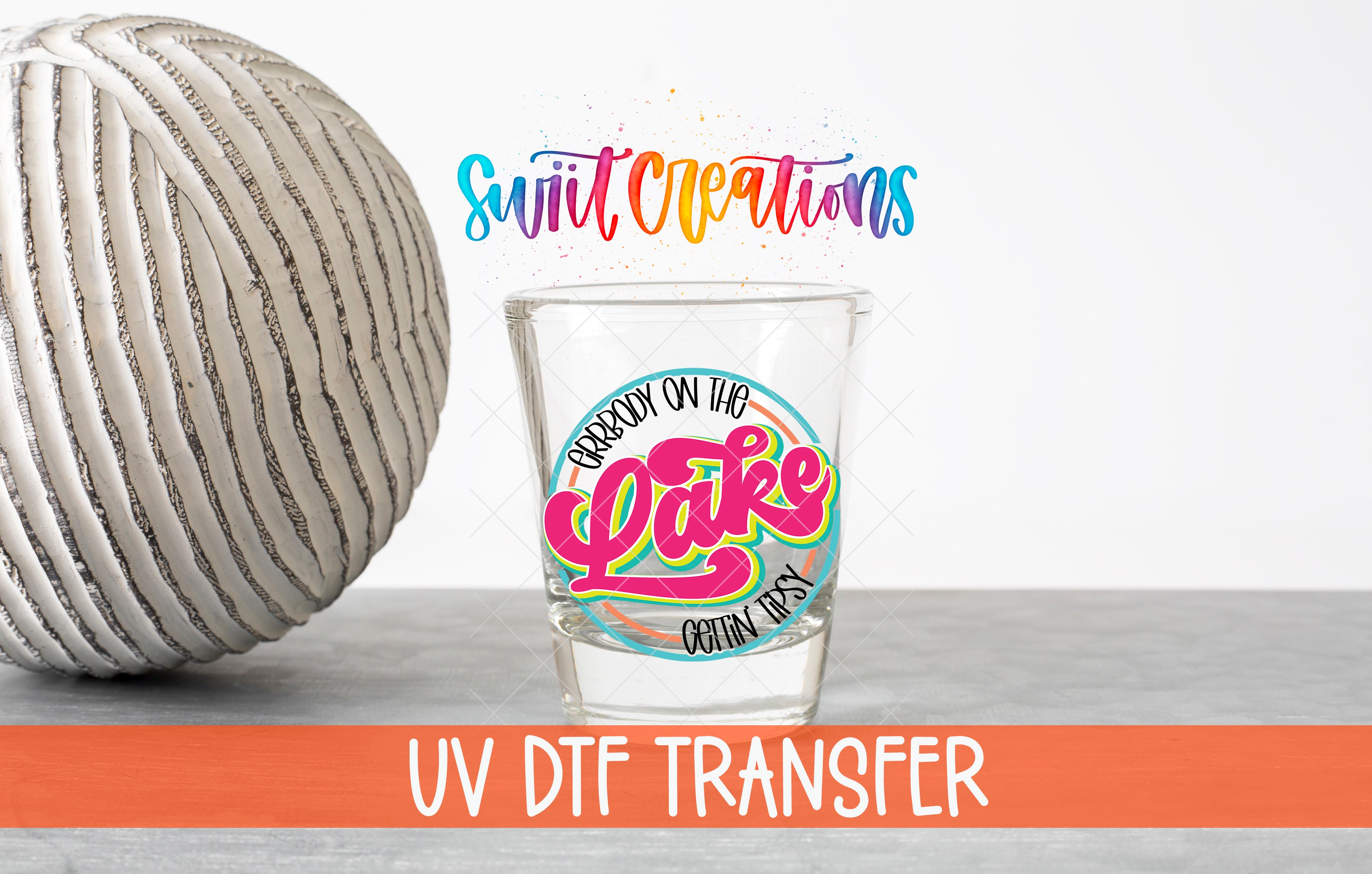 a shot glass with a colorful design and text, placed next to a gray ball on a table.