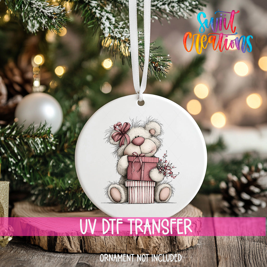 A white ceramic ornament with a teddy bear design is hanging on a Christmas tree.