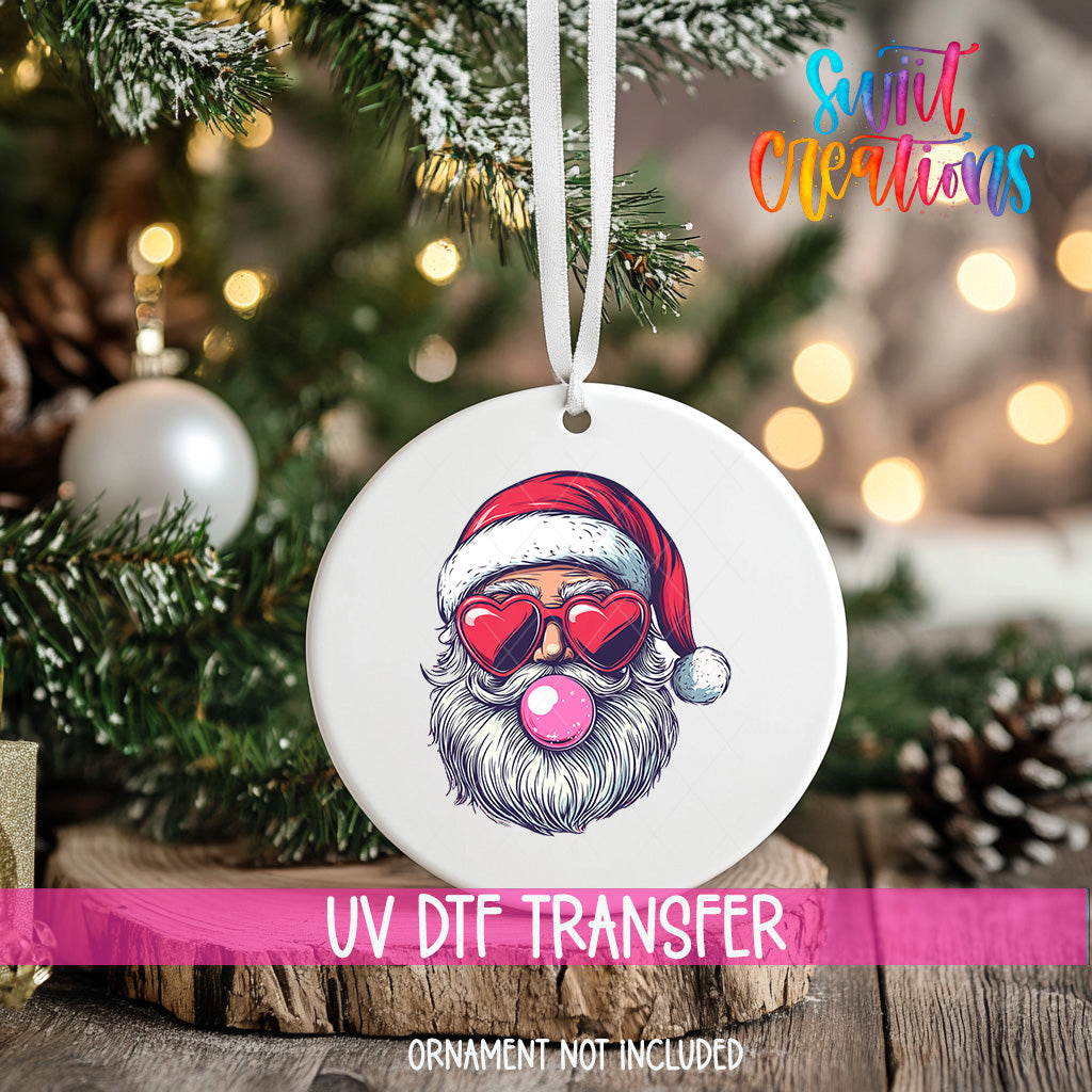 A white ornament with a Santa Claus face wearing sunglasses and a red hat is hanging on a Christmas tree.