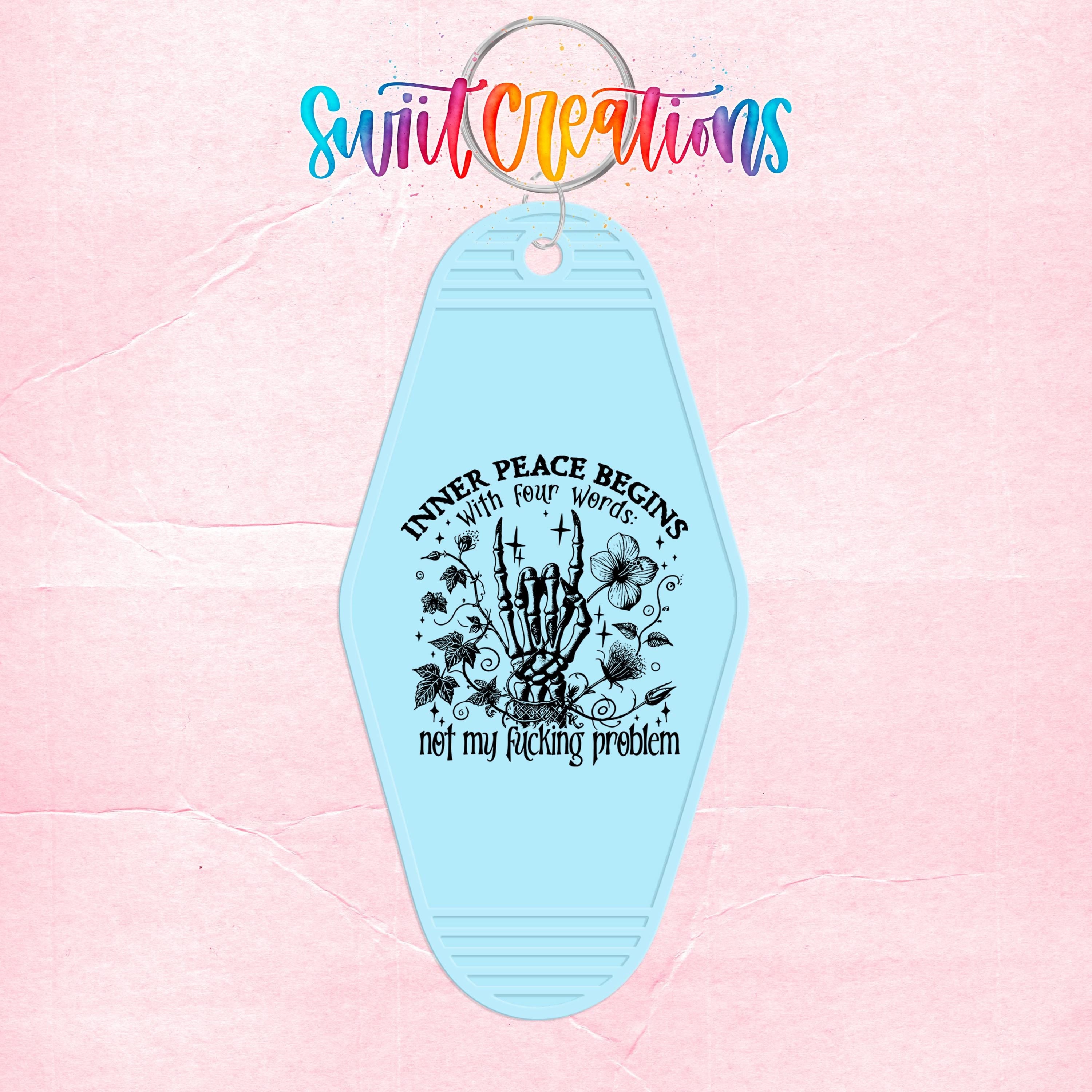 A keychain with a light blue design featuring a skeleton hand holding a flower and the text " Inner Peace Begins With Four Words Not My Fucking Problem".