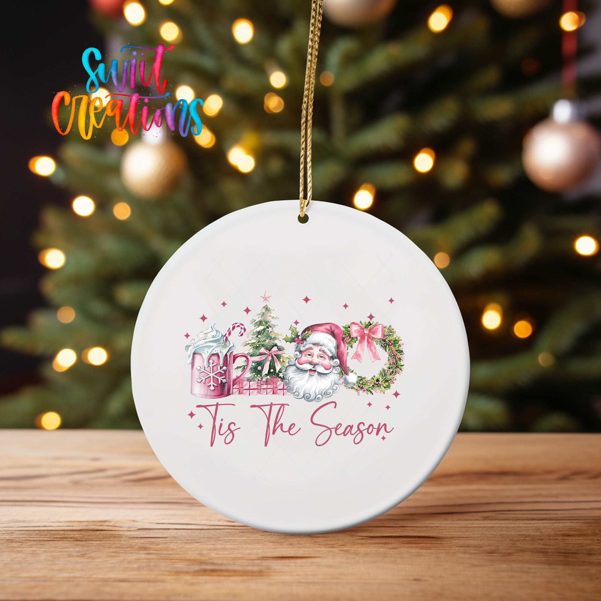 A white ceramic ornament with a Christmas tree and Santa Claus in the background, along with the text "Tis The Season" displayed on it.