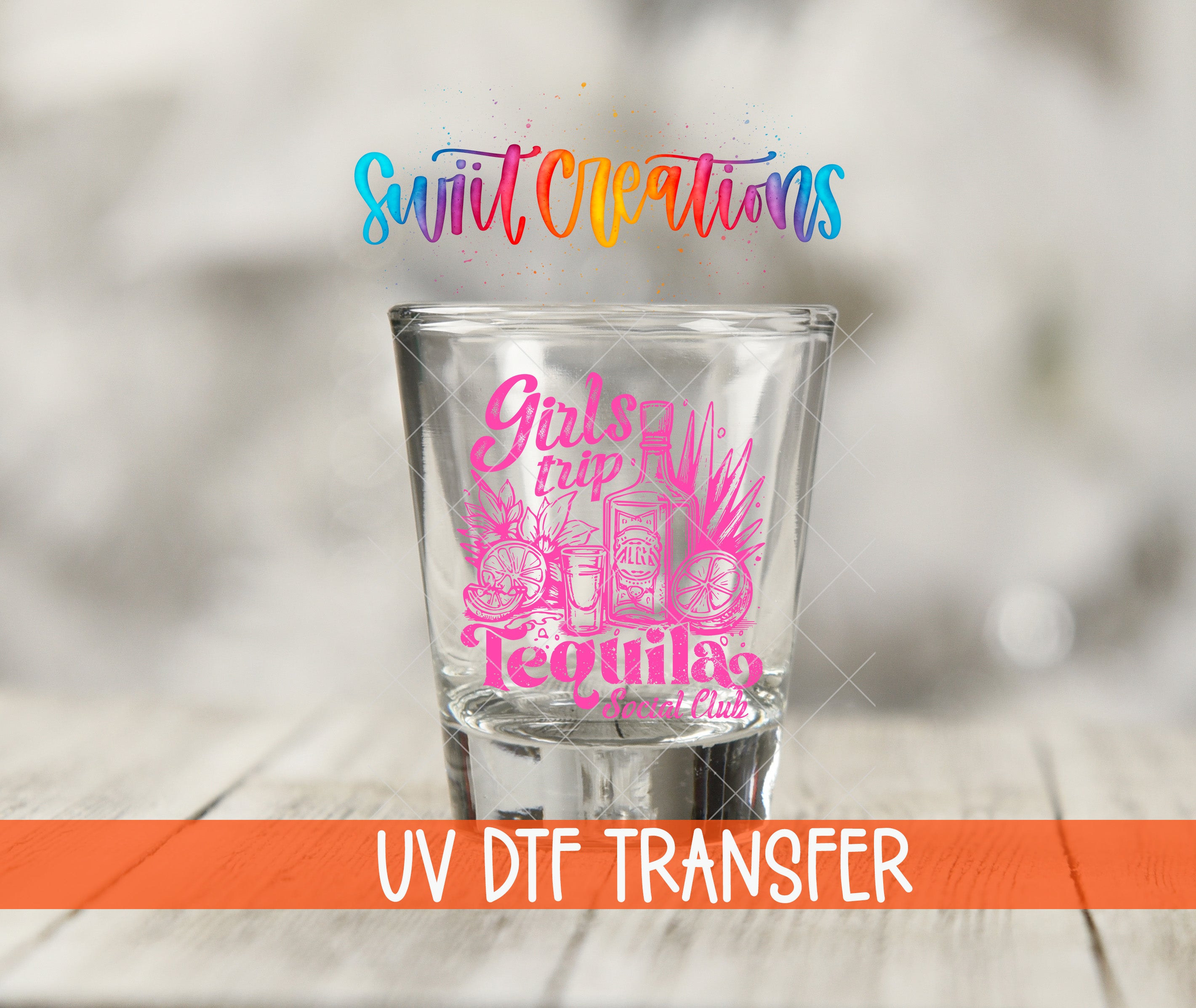 A shot glass with a pink design and text printed on it, placed on a wooden surface.