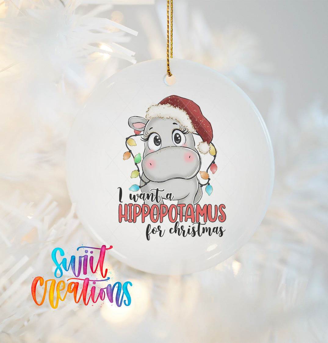 A white ornament with a cartoon image of a hippopotamus wearing a Santa hat and the text "I want a Hippopotamus for Christmas" hanging from a string.