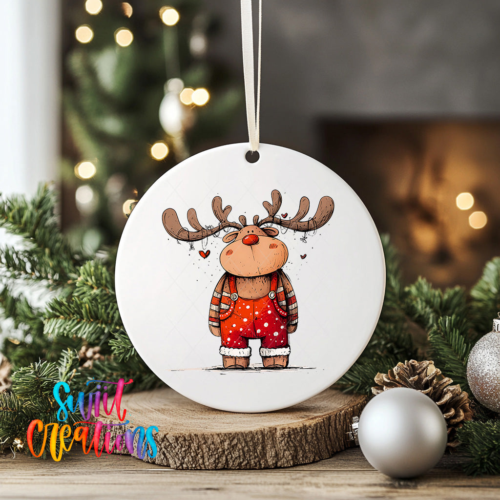 A white ornament featuring a cartoon reindeer wearing red overalls and antlers, surrounded by Christmas decorations such as pine cones and ornaments.