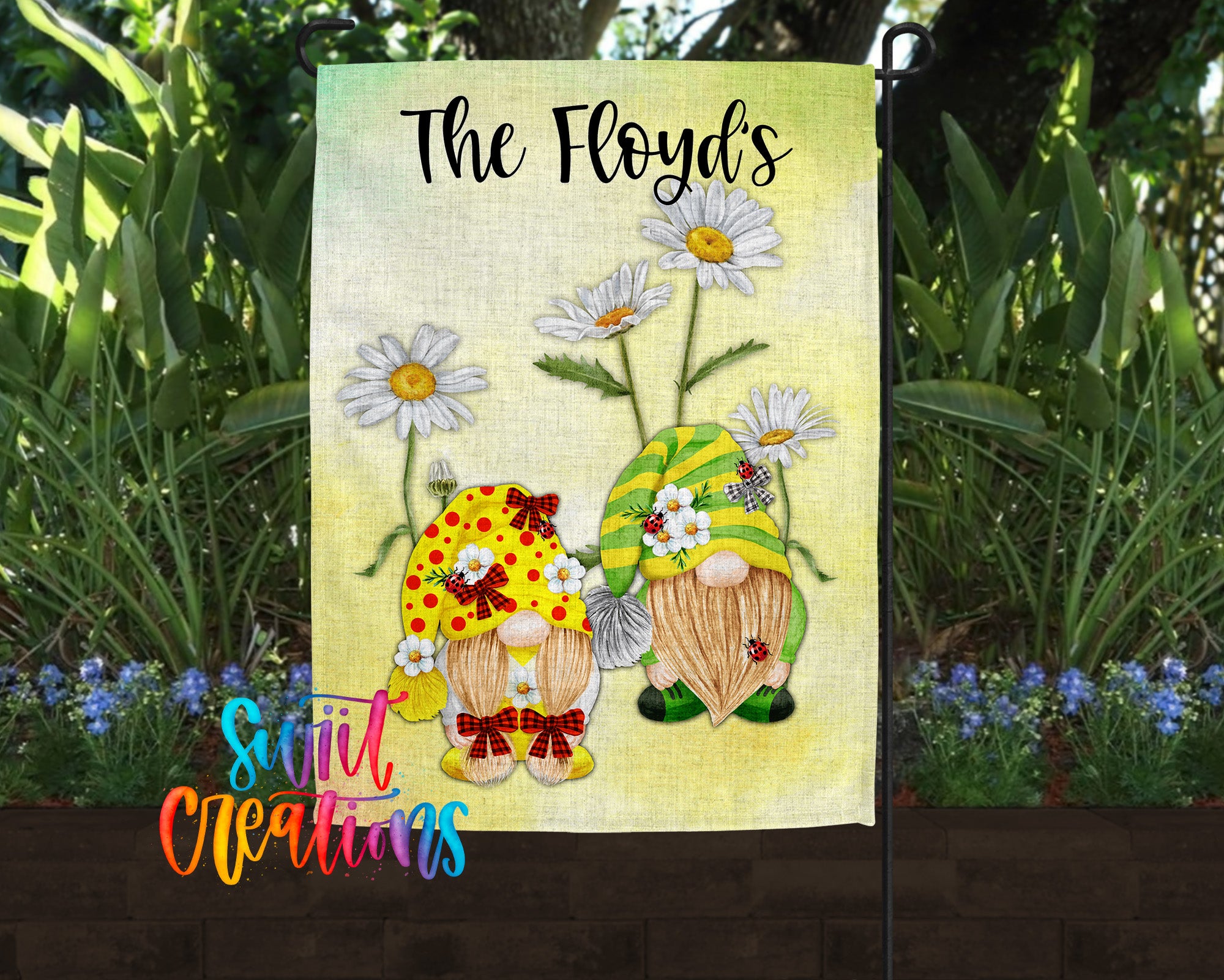 A garden flag featuring two gnomes with flower decorations, surrounded by greenery and flowers.