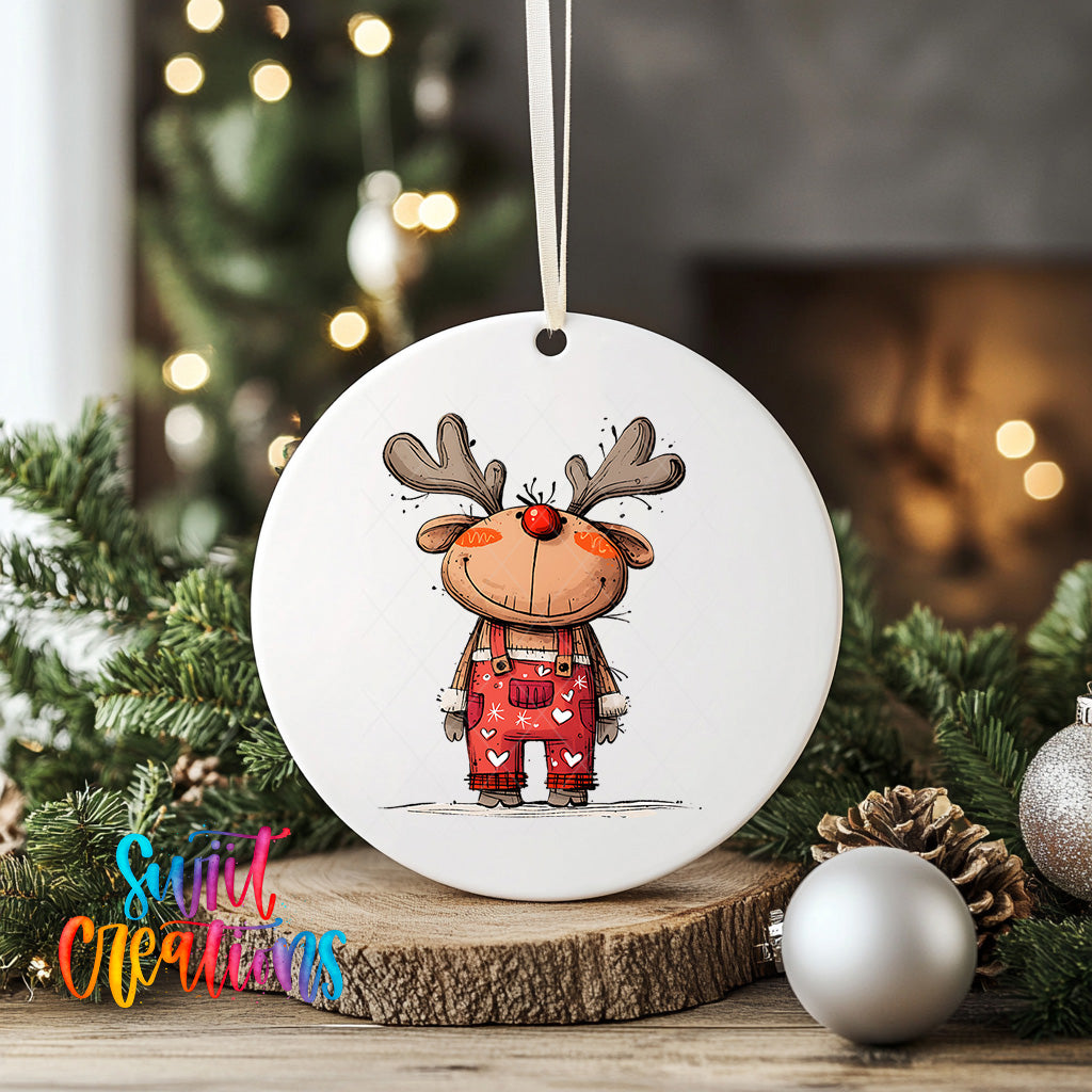 A white ceramic ornament featuring a cartoon reindeer wearing red overalls, standing on a wooden surface with Christmas decorations in the background.