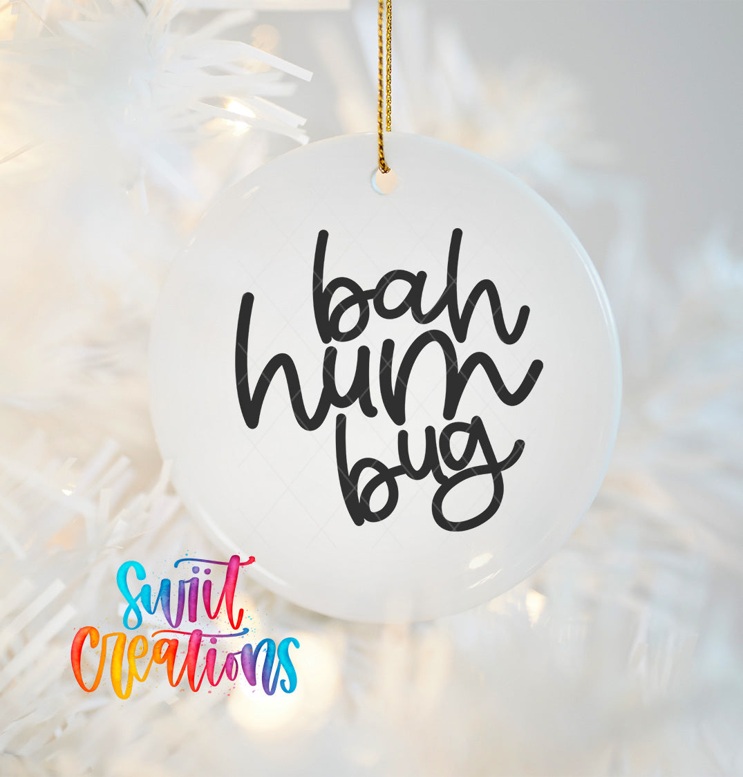 A white ornament with the text "bah hum bug" written on it, hanging on a Christmas tree.